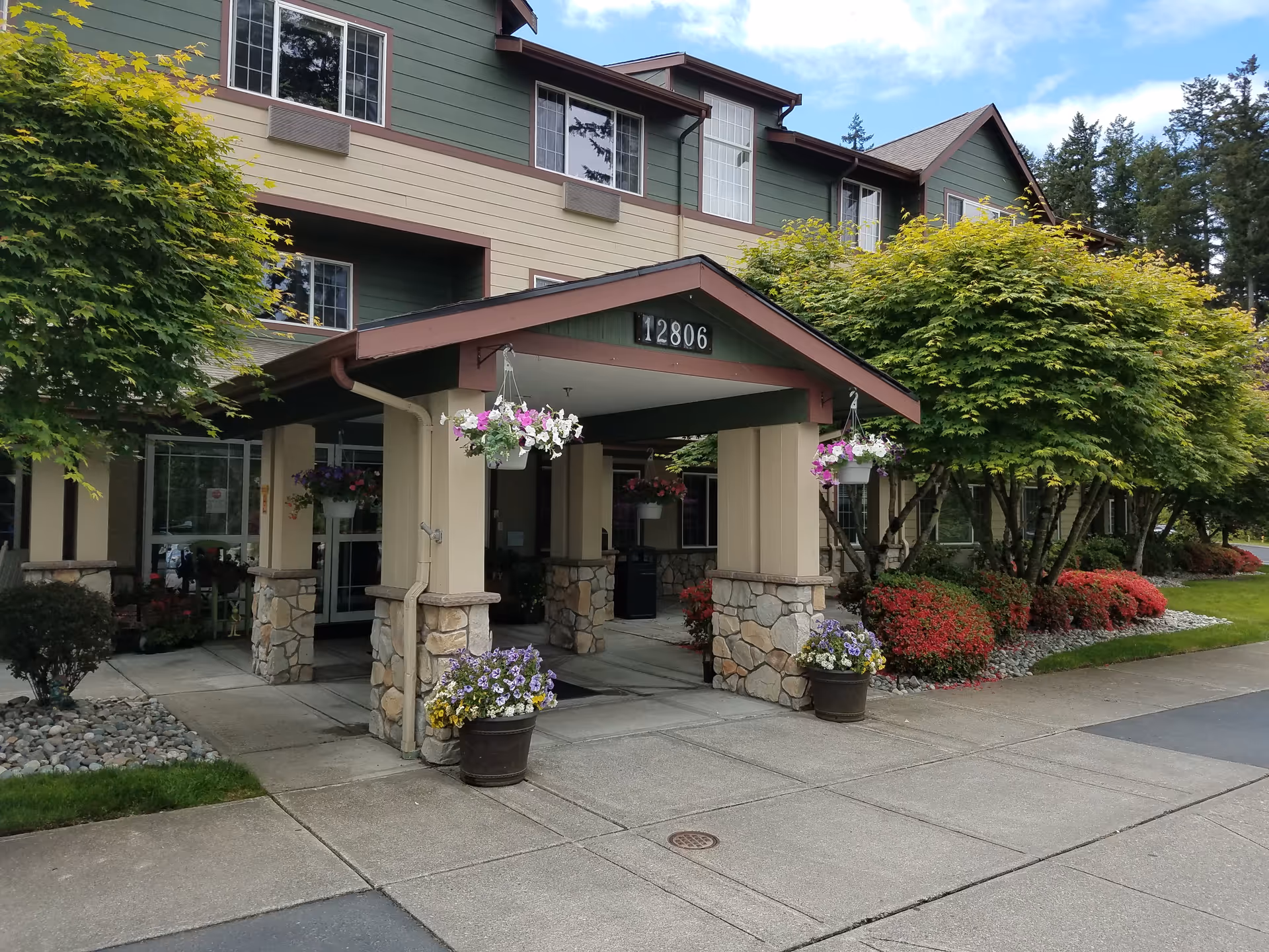 Exterior entrance of a senior living building with stone columns and hanging baskets.