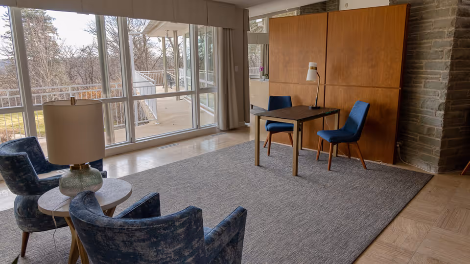 Bright indoor lounge at Yan Hospice with blue chairs, a desk, and large windows.