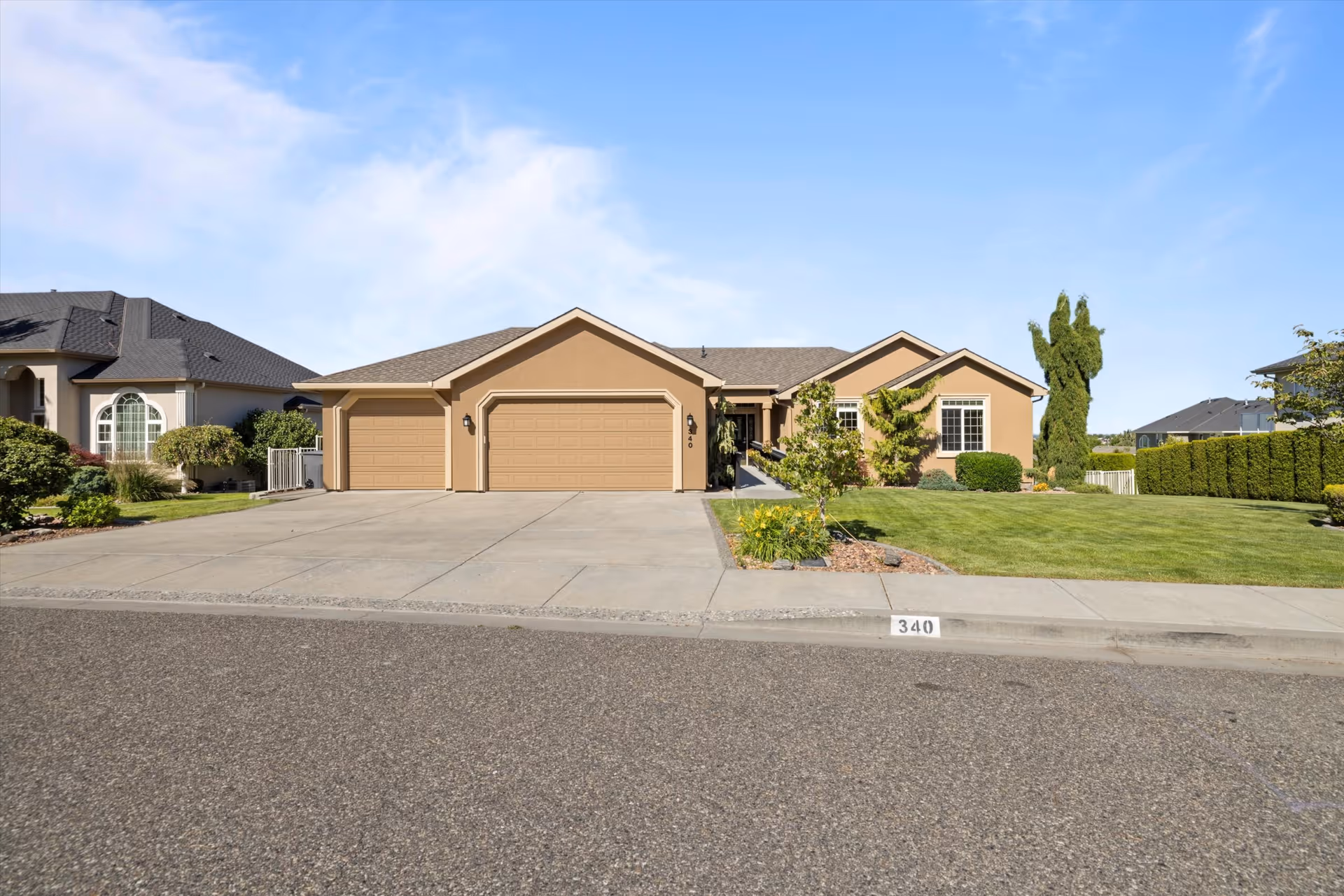 A tan, single-story residential building with a three-car garage and manicured front lawn along a suburban street.