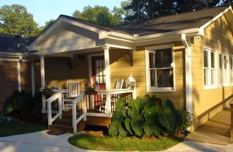 Yellow single-story senior living facility with a front porch and lush plants.