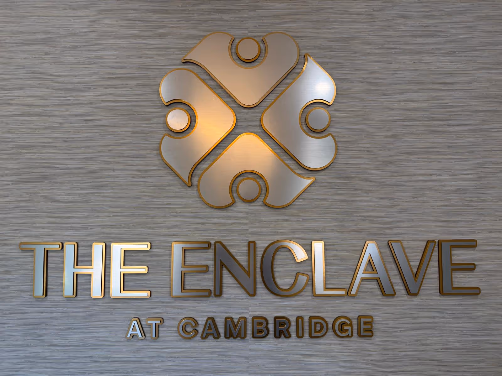 Metallic logo and THE ENCLAVE AT CAMBRIDGE sign mounted on a textured wall