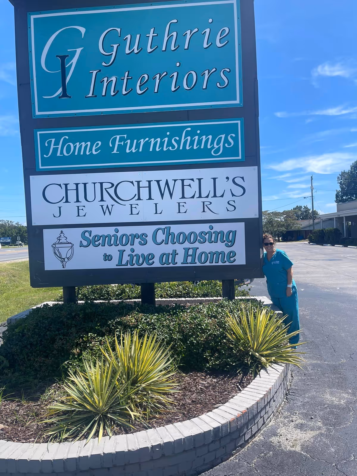 Outdoor sign displays Guthrie Interiors, Home Furnishings, Churchwell's Jewellers; a person in teal scrubs stands nearby.