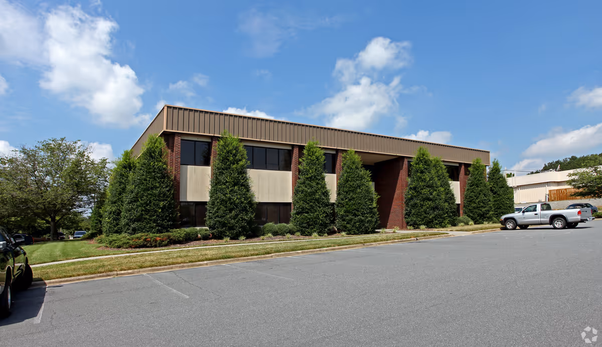 Exterior view of a brick office building with tall evergreen trees and a parking lot