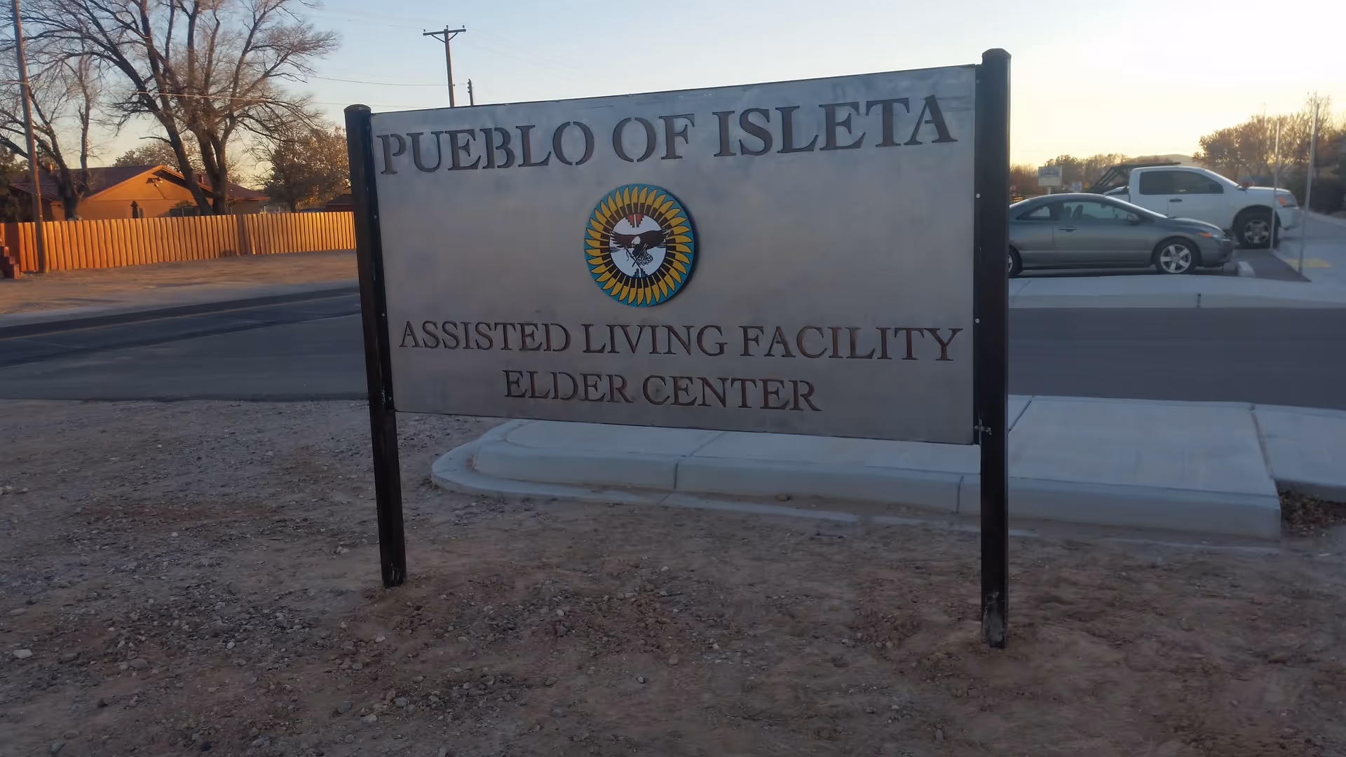 Exterior sign for Pueblo of Isleta Elder Center beside a street with parked cars