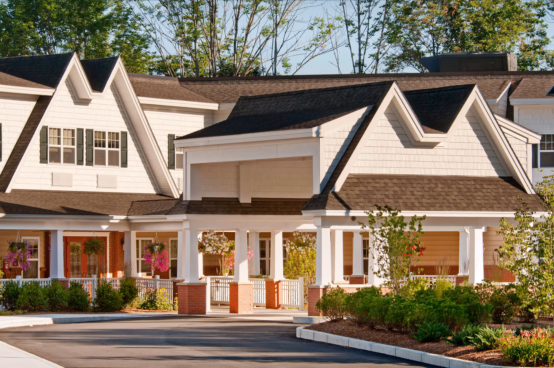 White-painted senior living facility with a covered entrance, columns, and landscaped shrubs.
