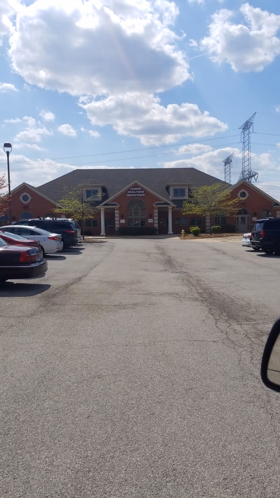 Exterior view of a brick dialysis care center with a parking lot and cars.