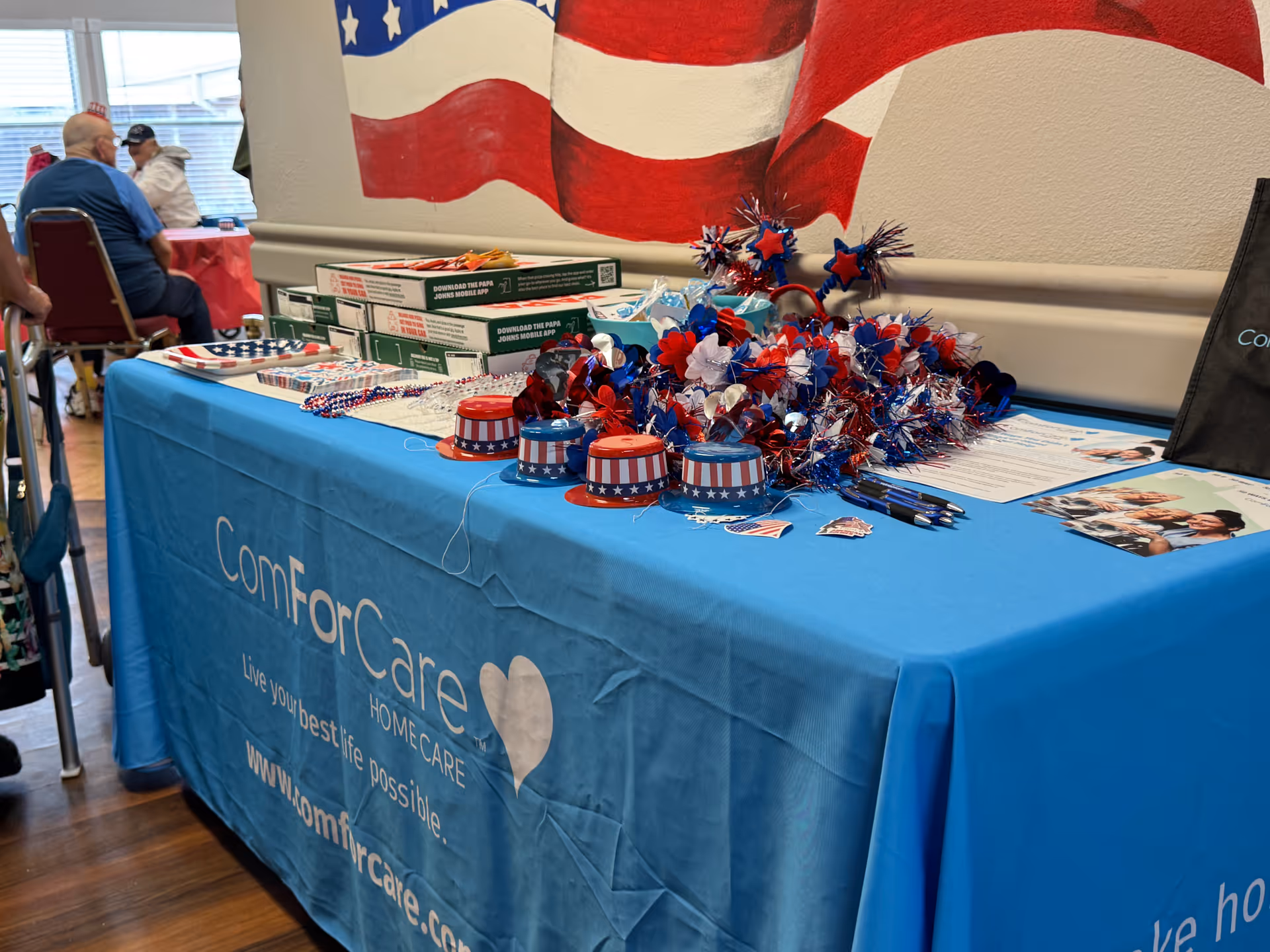 Promotional display table with ComForCare branding and patriotic decor inside a senior facility.