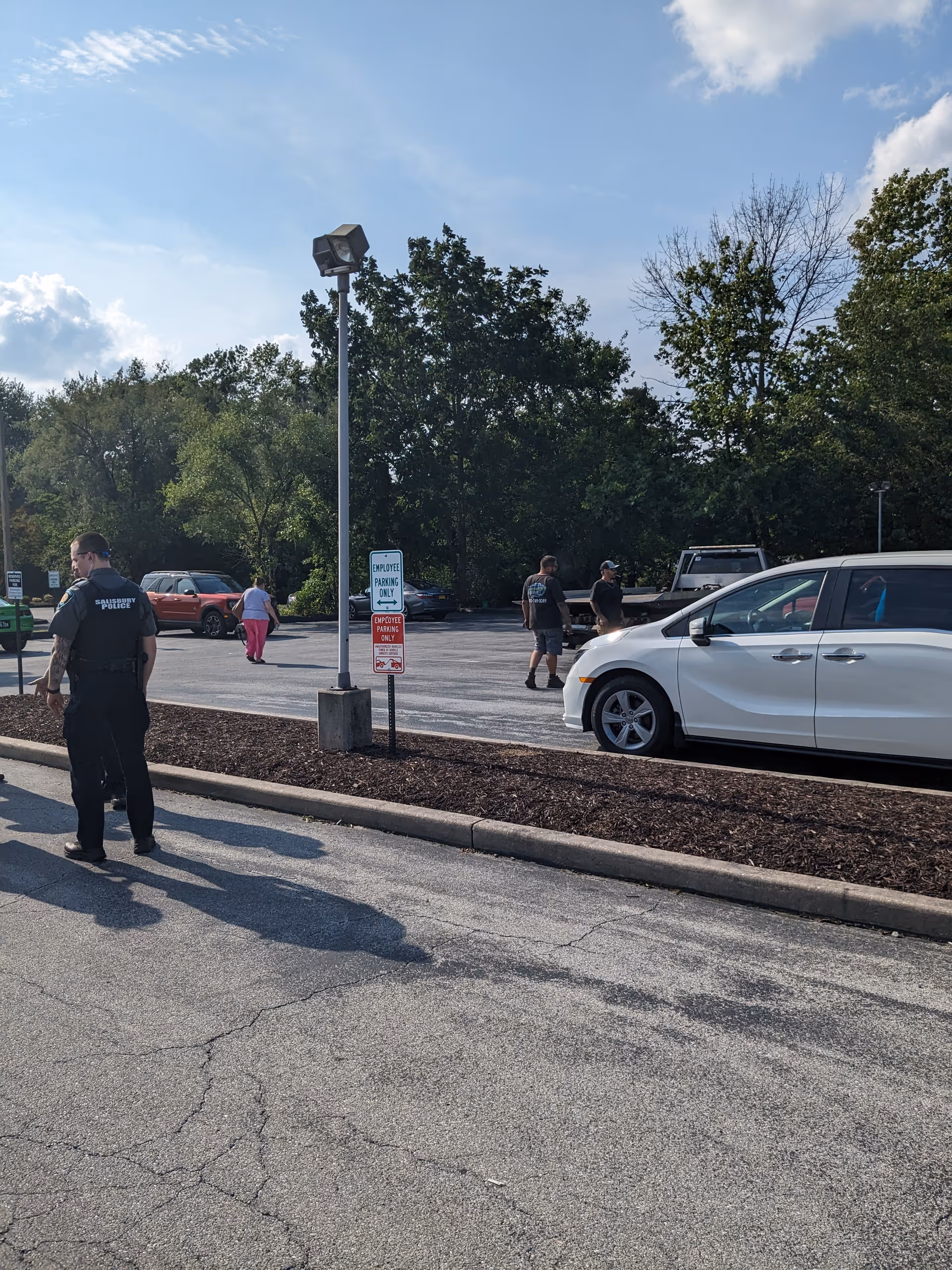 Outdoor parking lot outside a facility with several people and a white car.