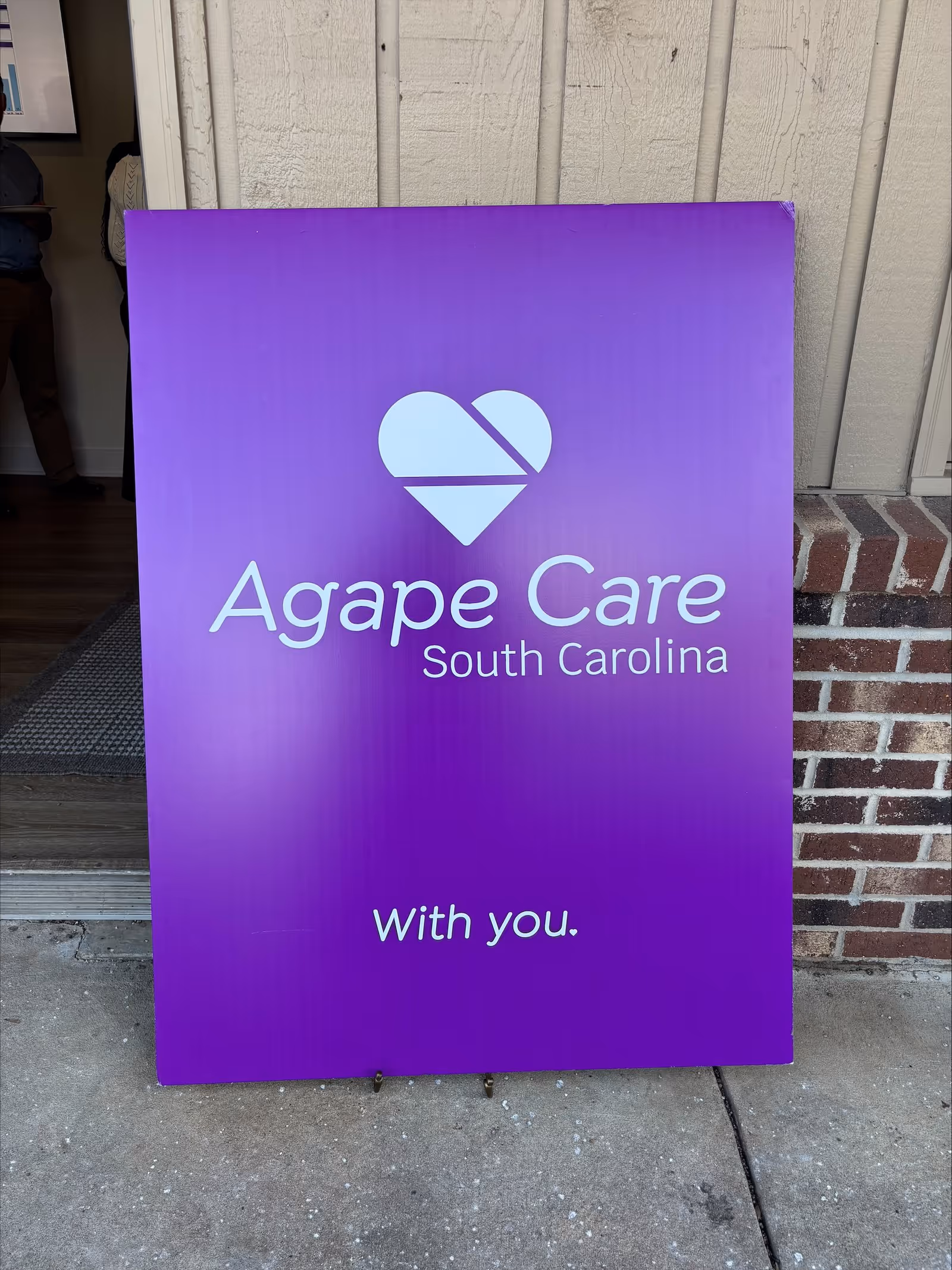 Purple Agape Care signboard outside a building entrance reading South Carolina and With you.
