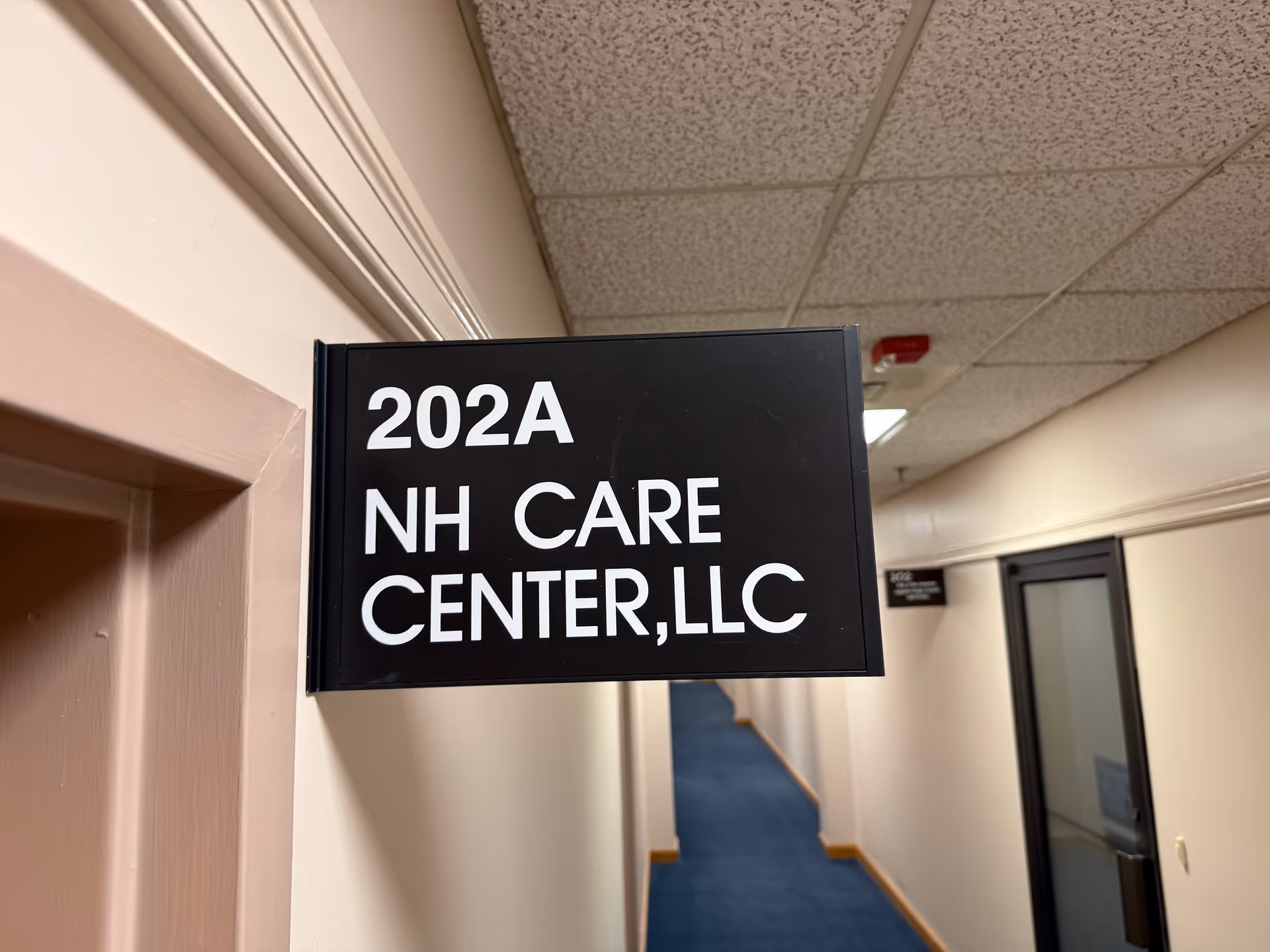 Black sign reading 202A NH CARE CENTER LLC in a hallway.