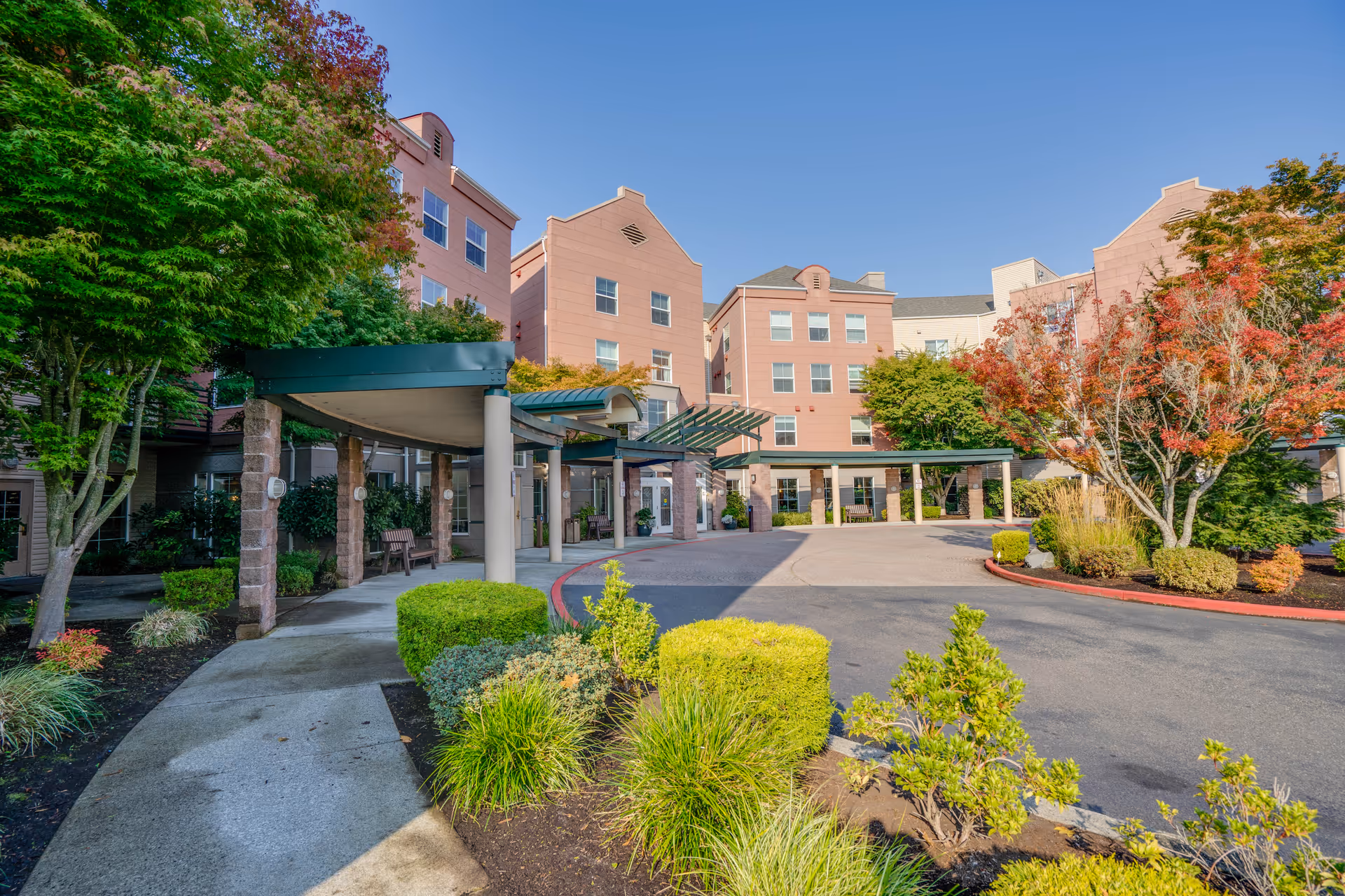 Front entrance and circular driveway of a multi-story retirement community building with a covered porte-cochère and landscaped grounds.