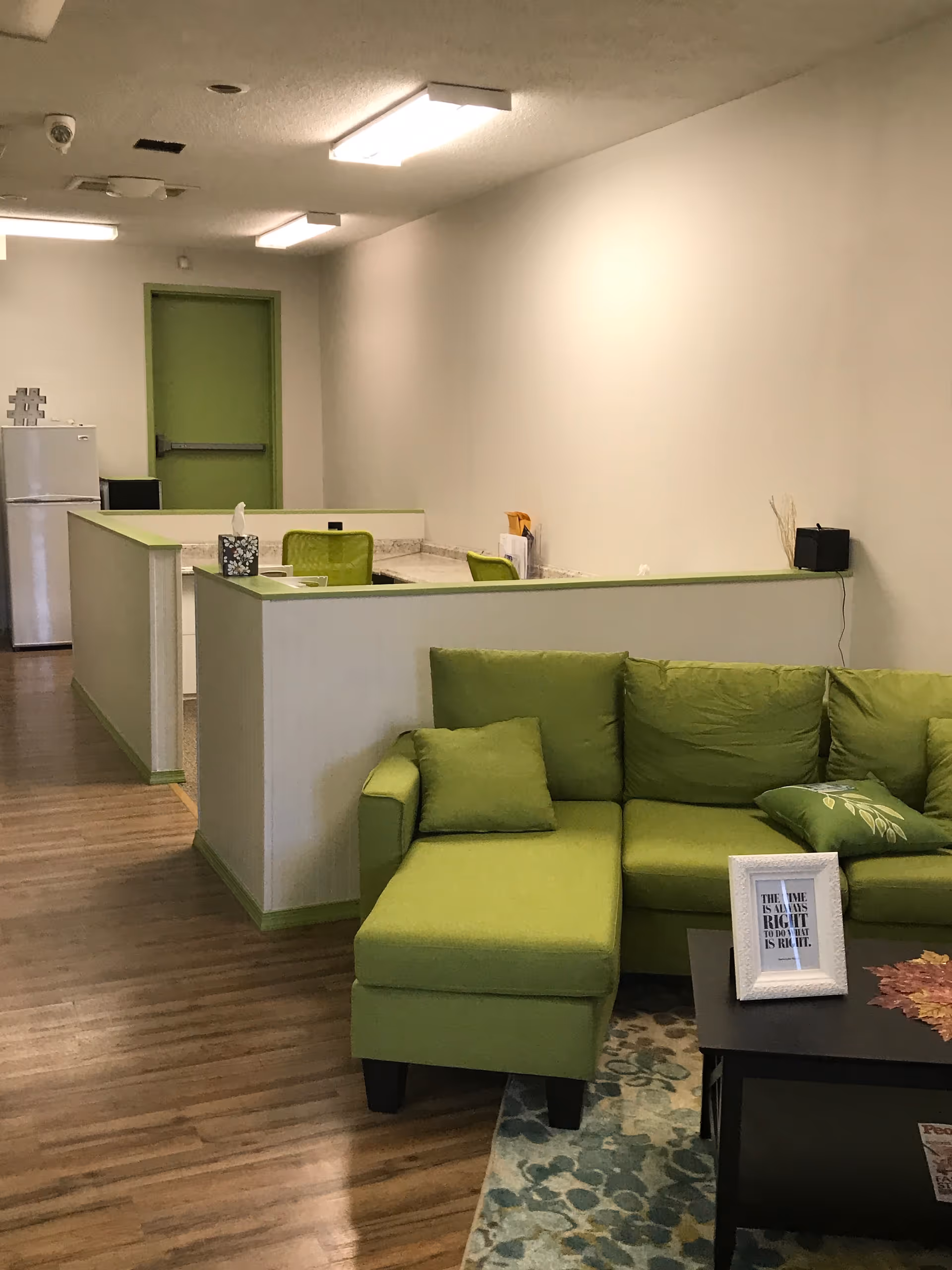 Bright lobby area with a green sofa, partitions, and a small coffee table.