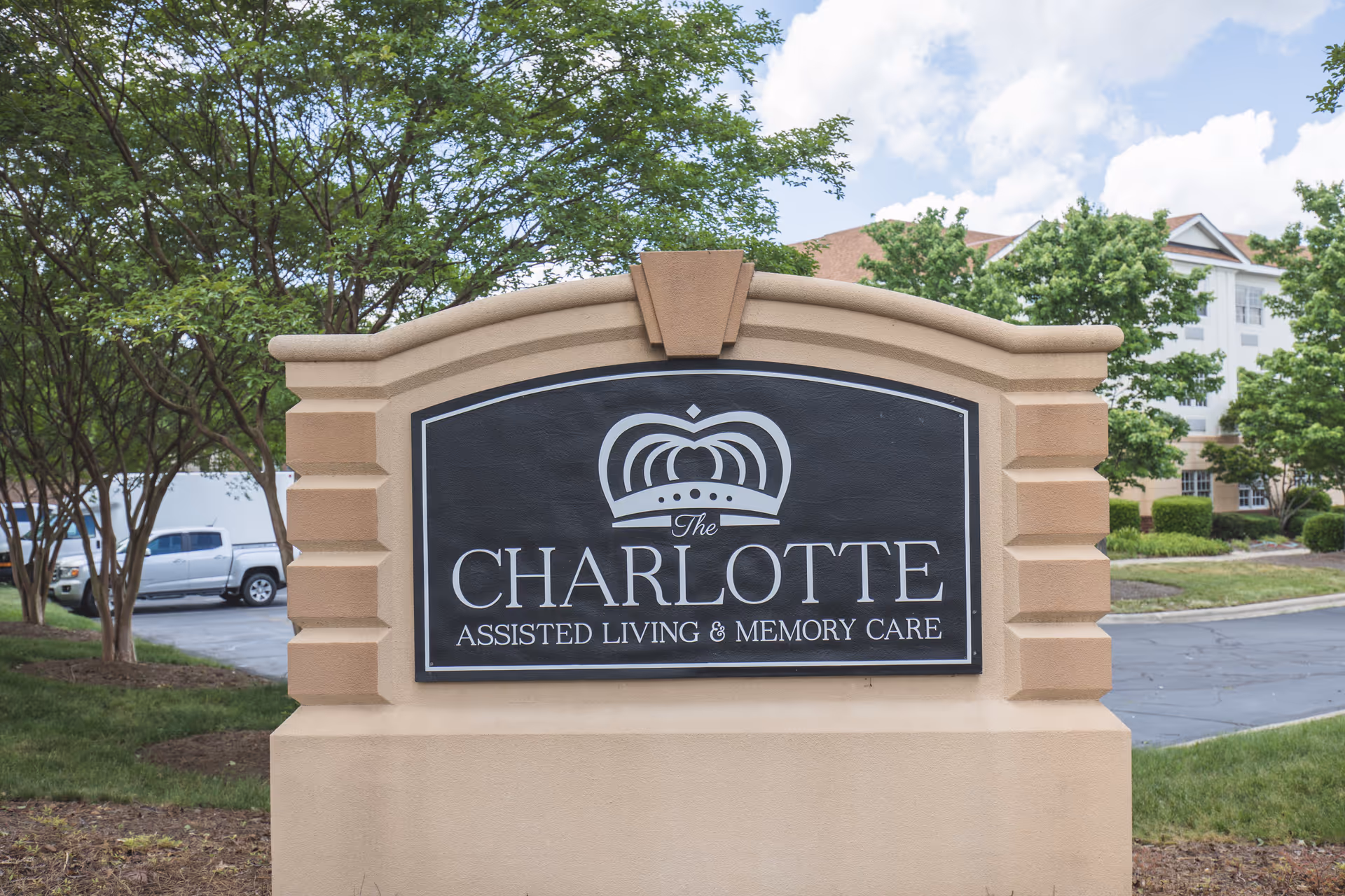 Beige stone sign for The Charlotte Assisted Living & Memory Care in front of trees