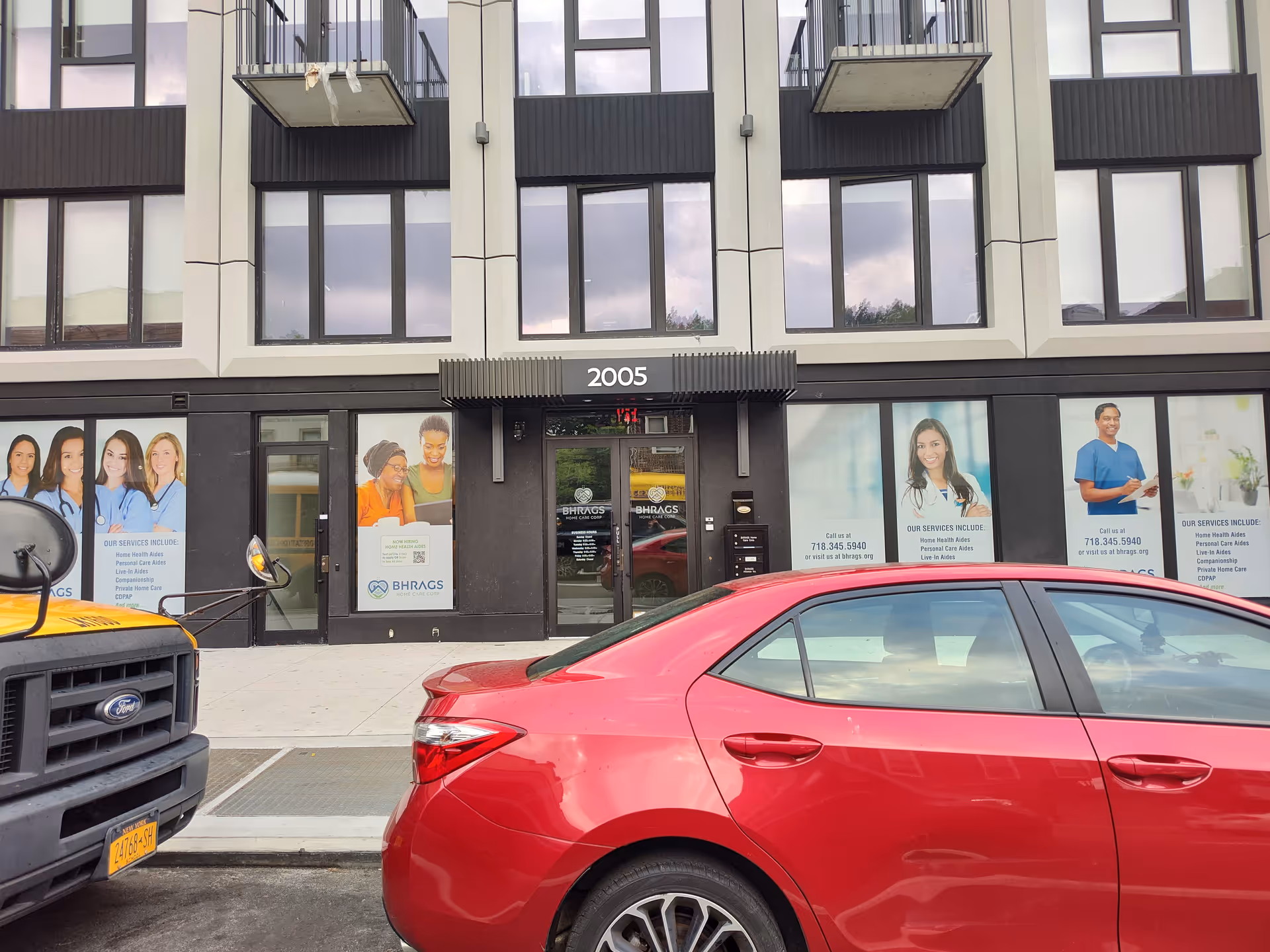 Exterior facade of a modern building with large windows, storefronts, and parked cars.