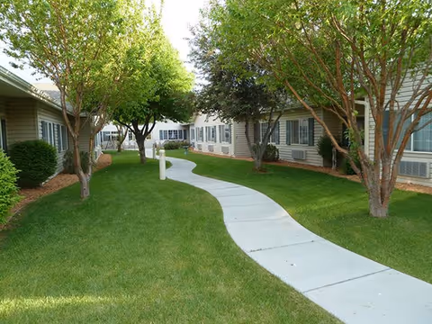 Curved concrete walkway winds through green lawn between senior living buildings with trees.