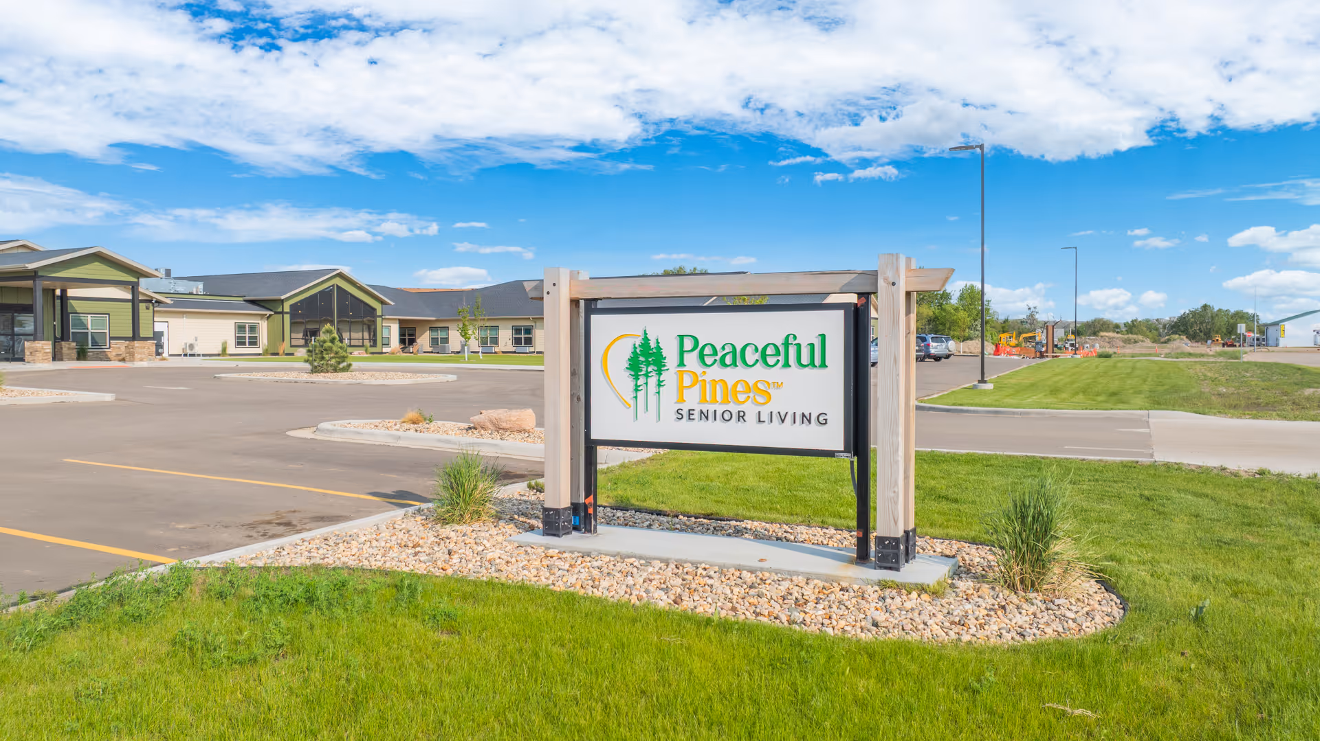 Exterior view of Peaceful Pines Senior Living sign with building and parking lot.