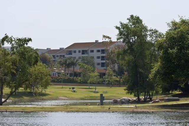 Exterior view of Regents Point campus across a lake with trees and green lawn.