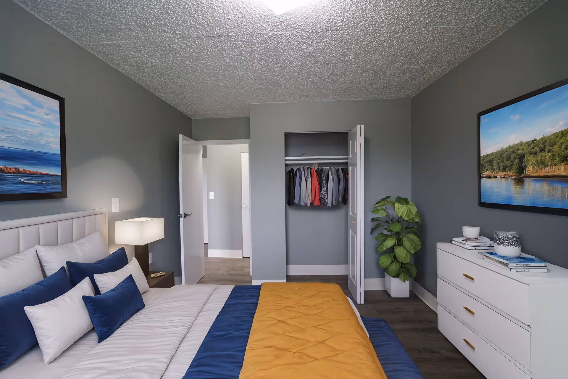 A modern bedroom with a neatly made bed, dresser, closet, and wall art.