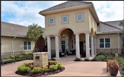 Exterior view of a beige senior living facility with arched entrance and columns