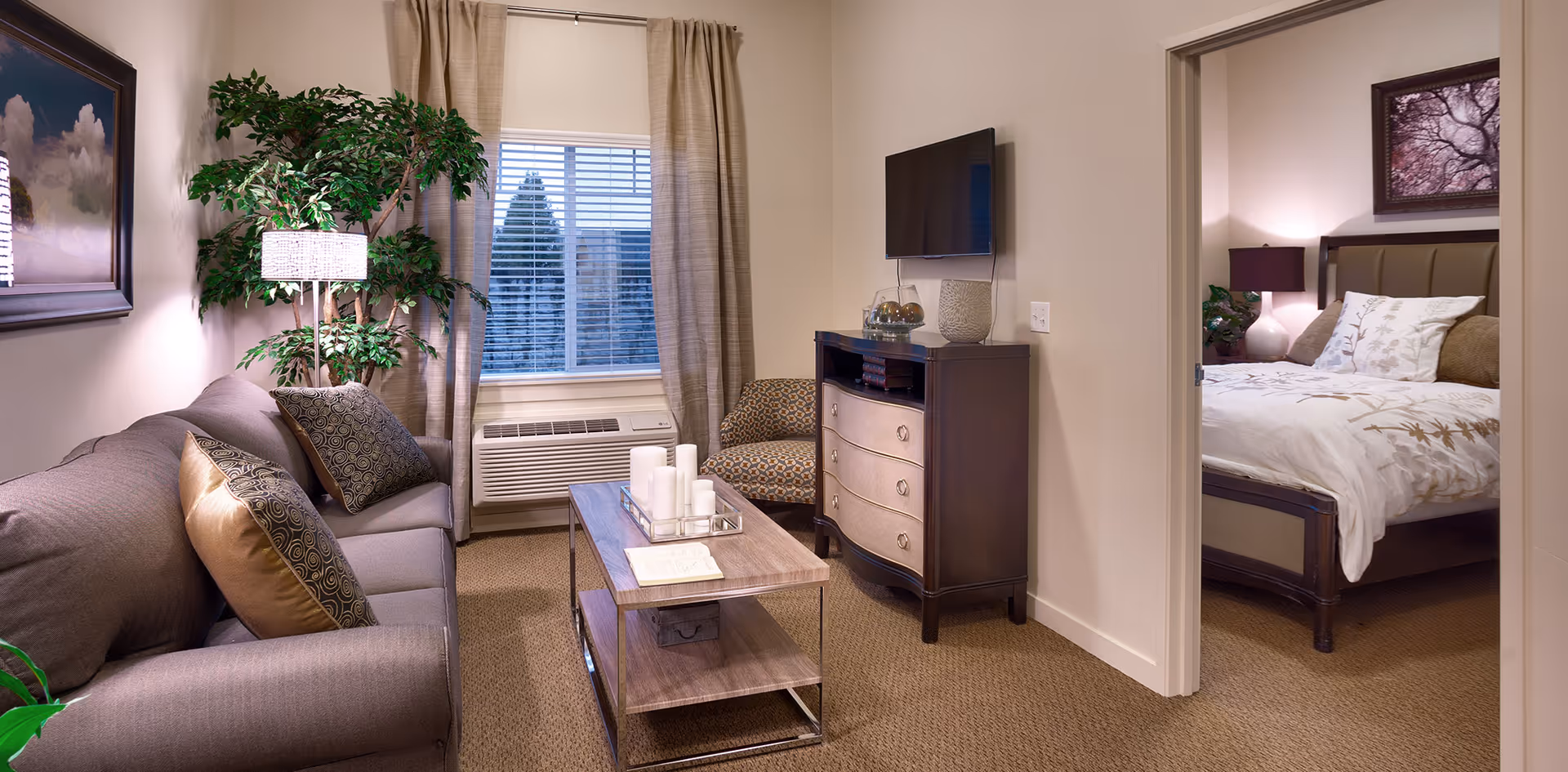 Cozy living room with a sofa, coffee table, TV cabinet, and a doorway revealing the adjacent bedroom.