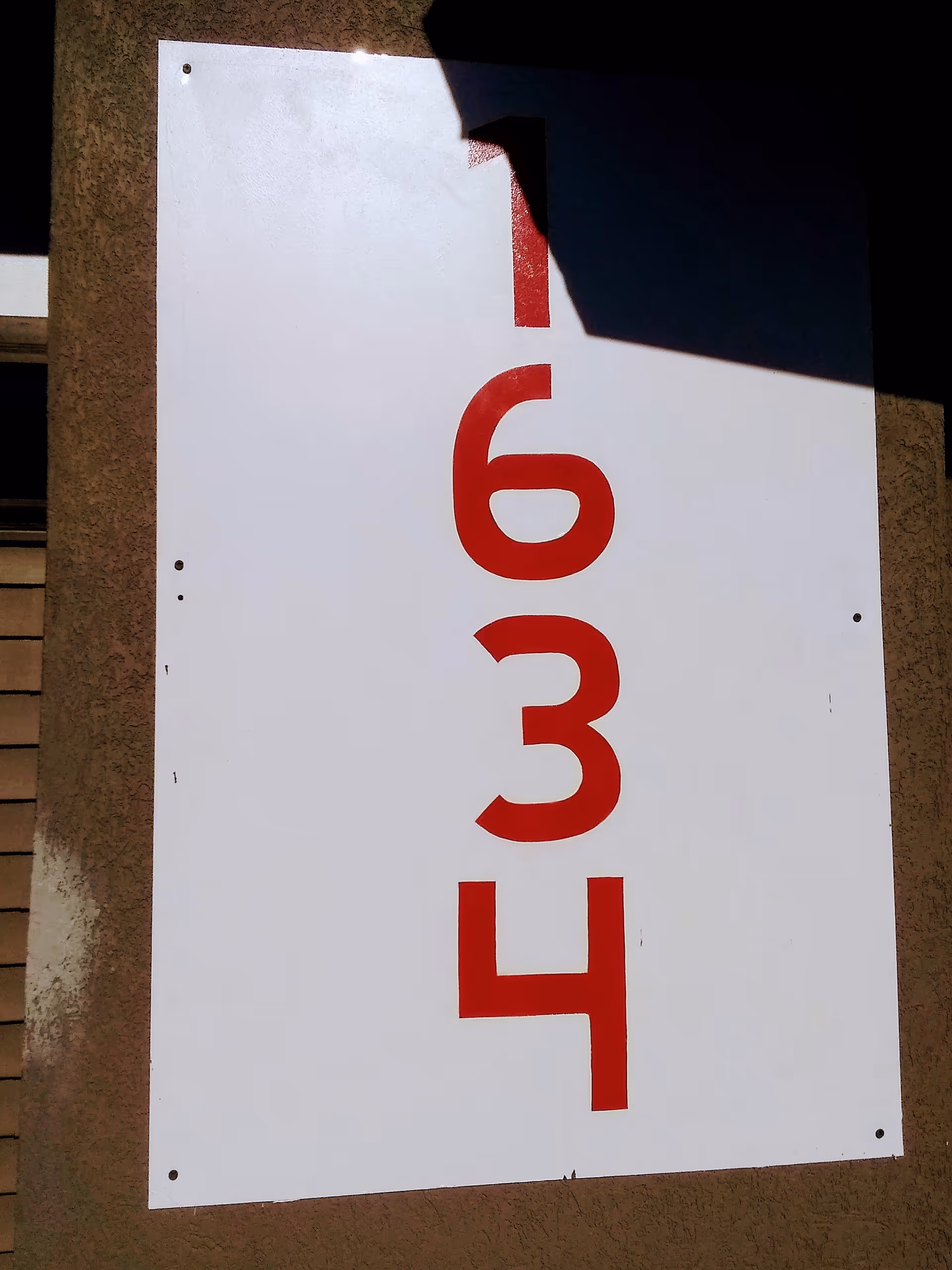 White sign with red vertical numbers 6 3 4 mounted on an exterior wall.
