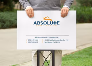 Person holds a large sign for Absolute Home Health outdoors near a walkway.