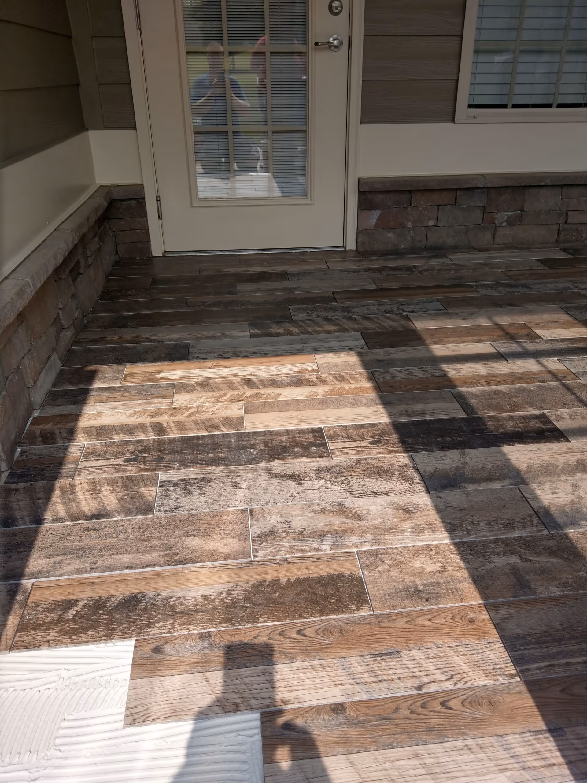 Exterior entry with a glass door, stone veneer wall, and wood-looking tile porch.