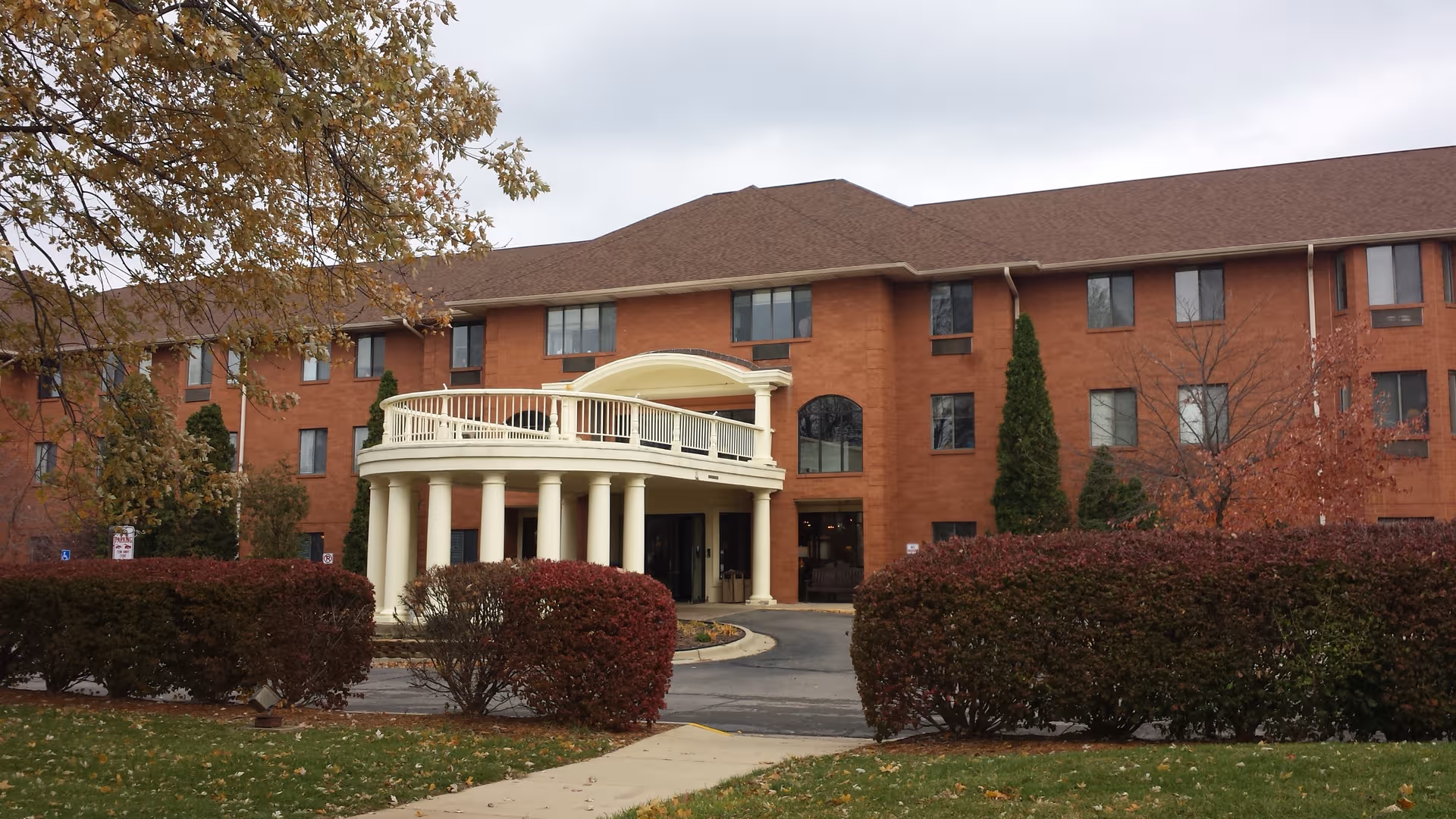 Brick senior living building with a circular portico and manicured hedges at the entrance.