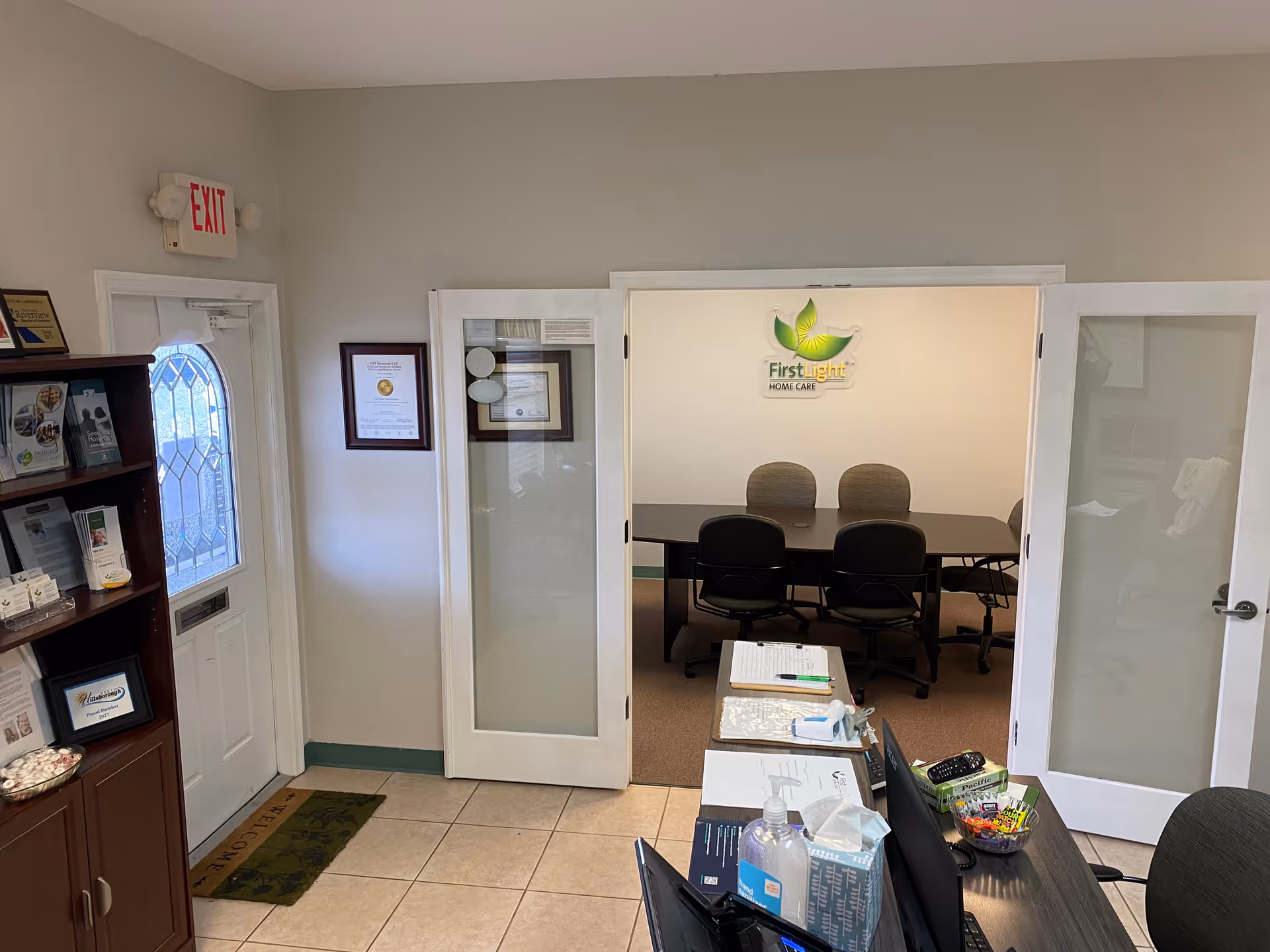 Office reception area with front desk, glass doors, and conference room featuring FirstLight Home Care logo.