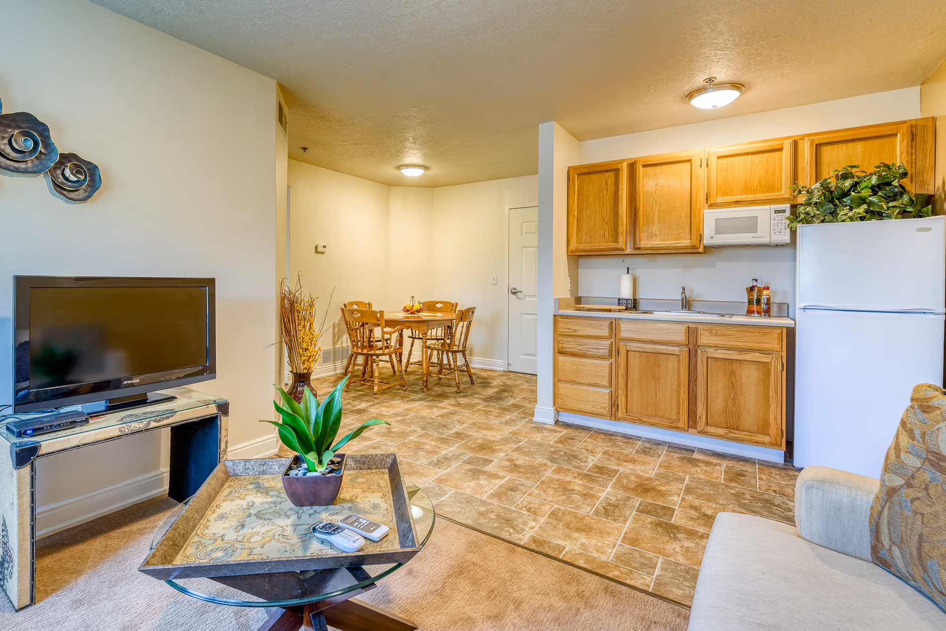 Open-concept living area with TV, coffee table, kitchen cabinets, fridge, and dining table.