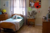 A cozy resident bedroom with bed, dresser, nightstand, fan, and a stuffed toy.