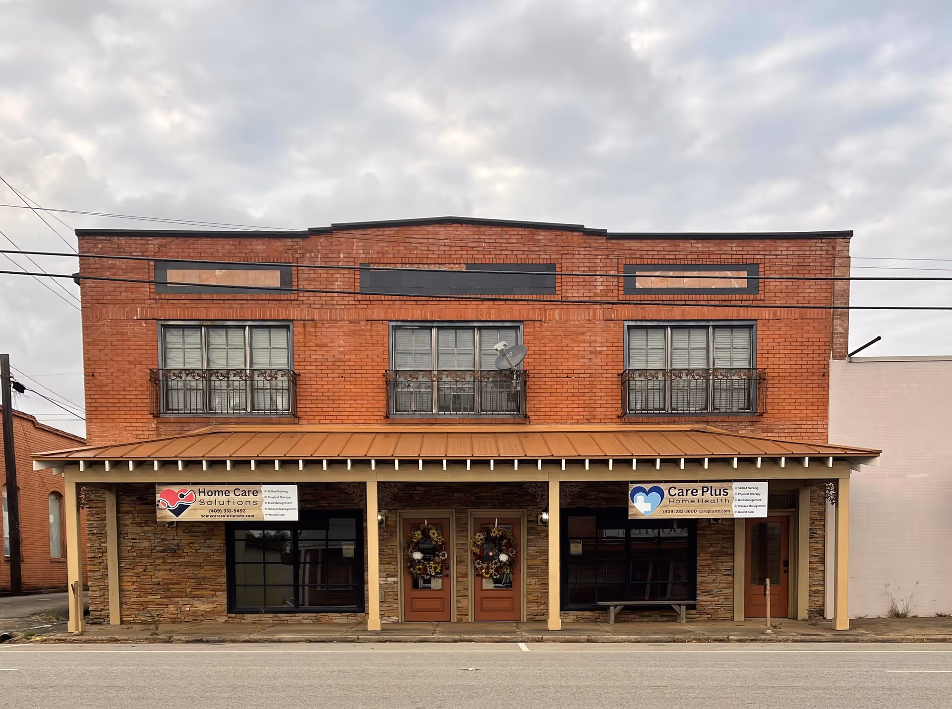 Two-story brick building with storefronts, wreaths on doors, and banners for Home Care Solutions.