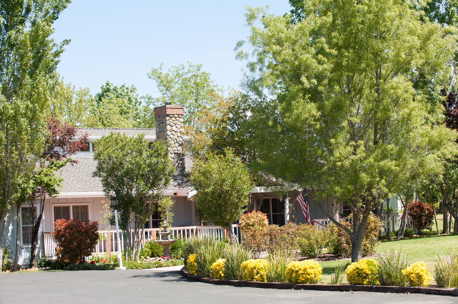 A senior living facility entrance with lush trees, shrubs, and an American flag.