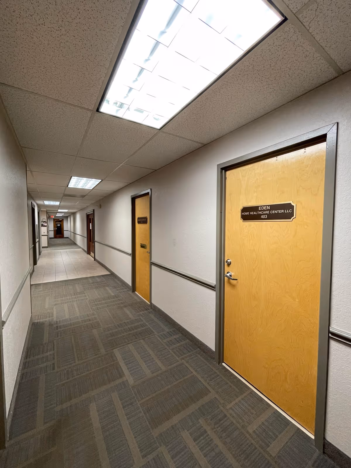 Long hallway in a senior care facility with wood doors and bright ceiling lights.