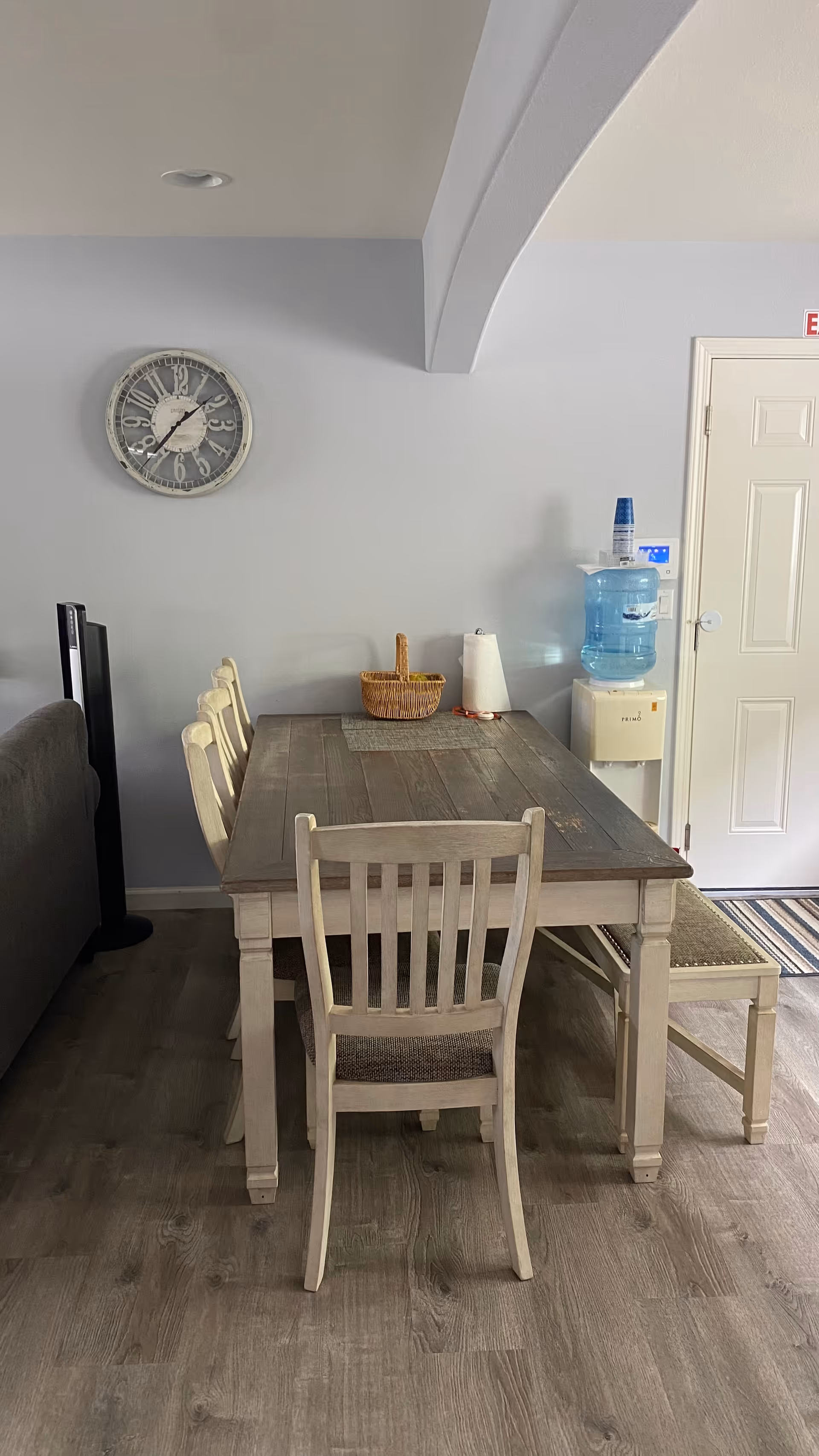 Wood dining table with chairs in a light blue dining area, wall clock visible.