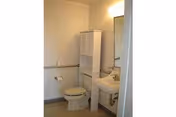 Small bathroom in a senior living facility with toilet, sink, mirror and cabinet.