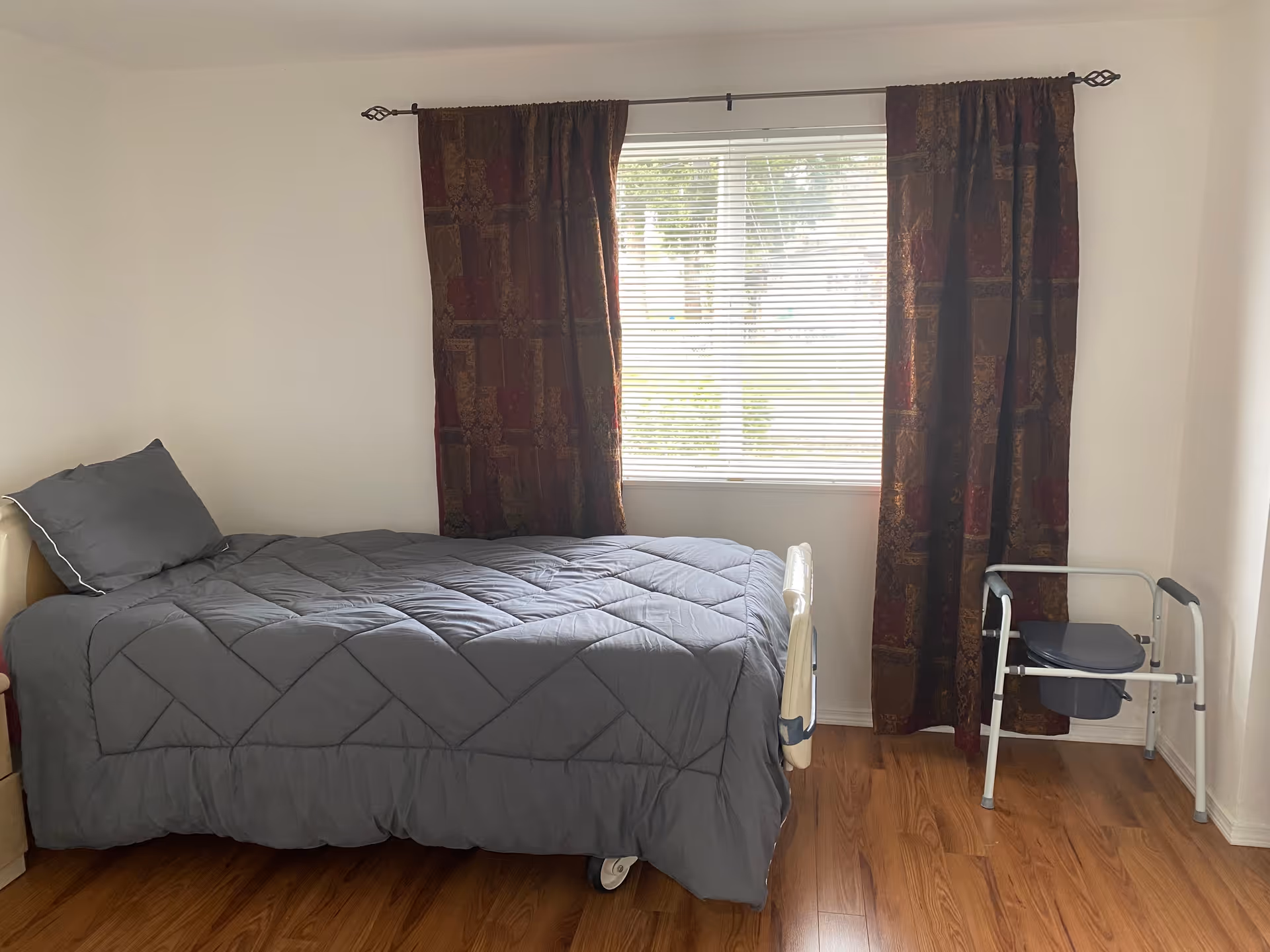 A bedroom with a bed, window, patterned curtains, and a walker nearby.