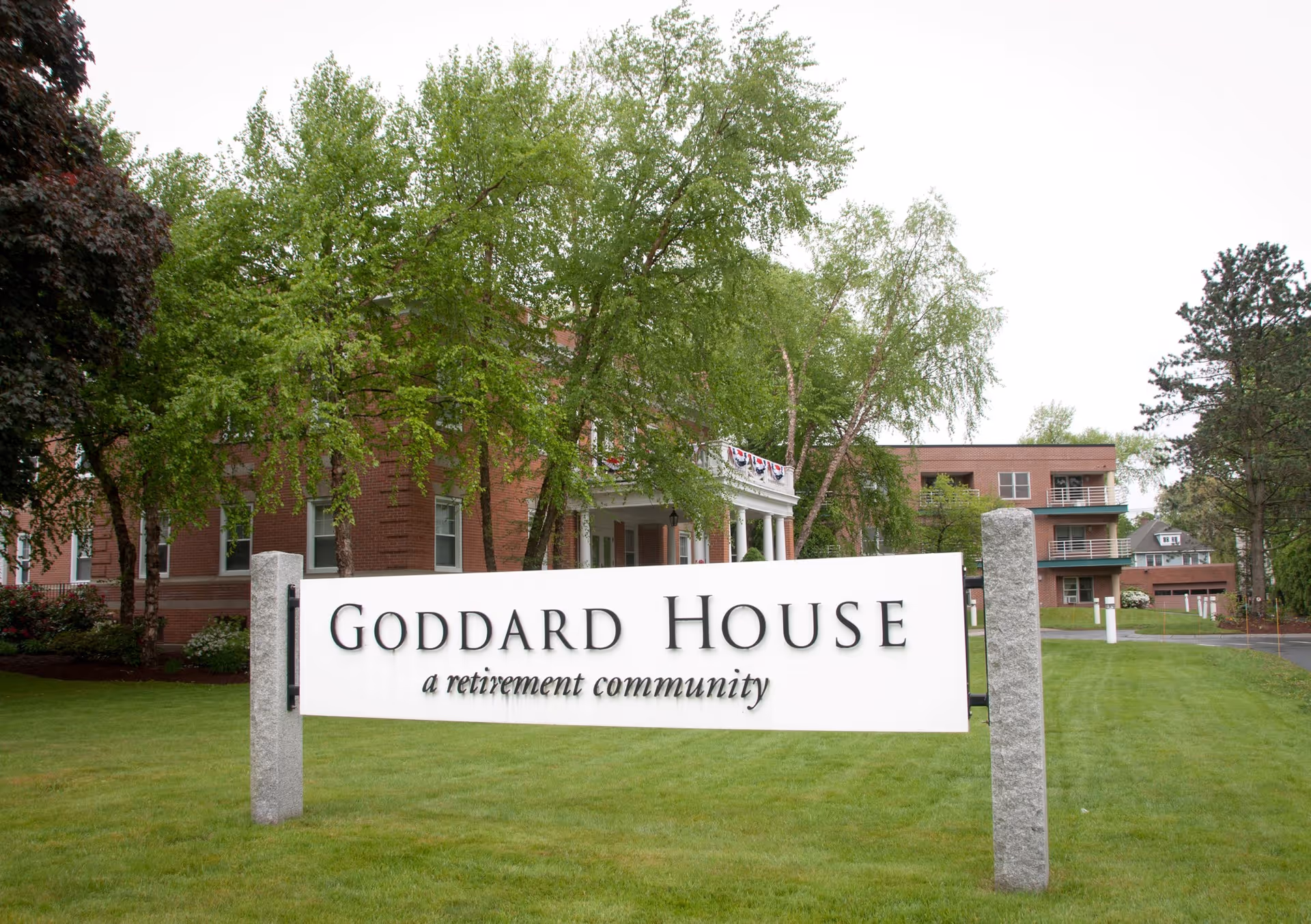 Goddard House retirement community sign in front of a brick building with trees.