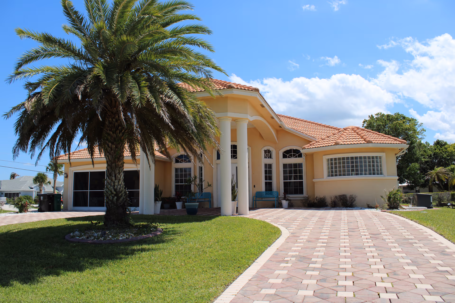 Sunny front view of Avalon Family Resort senior living facility with palm trees and tiled walkway.