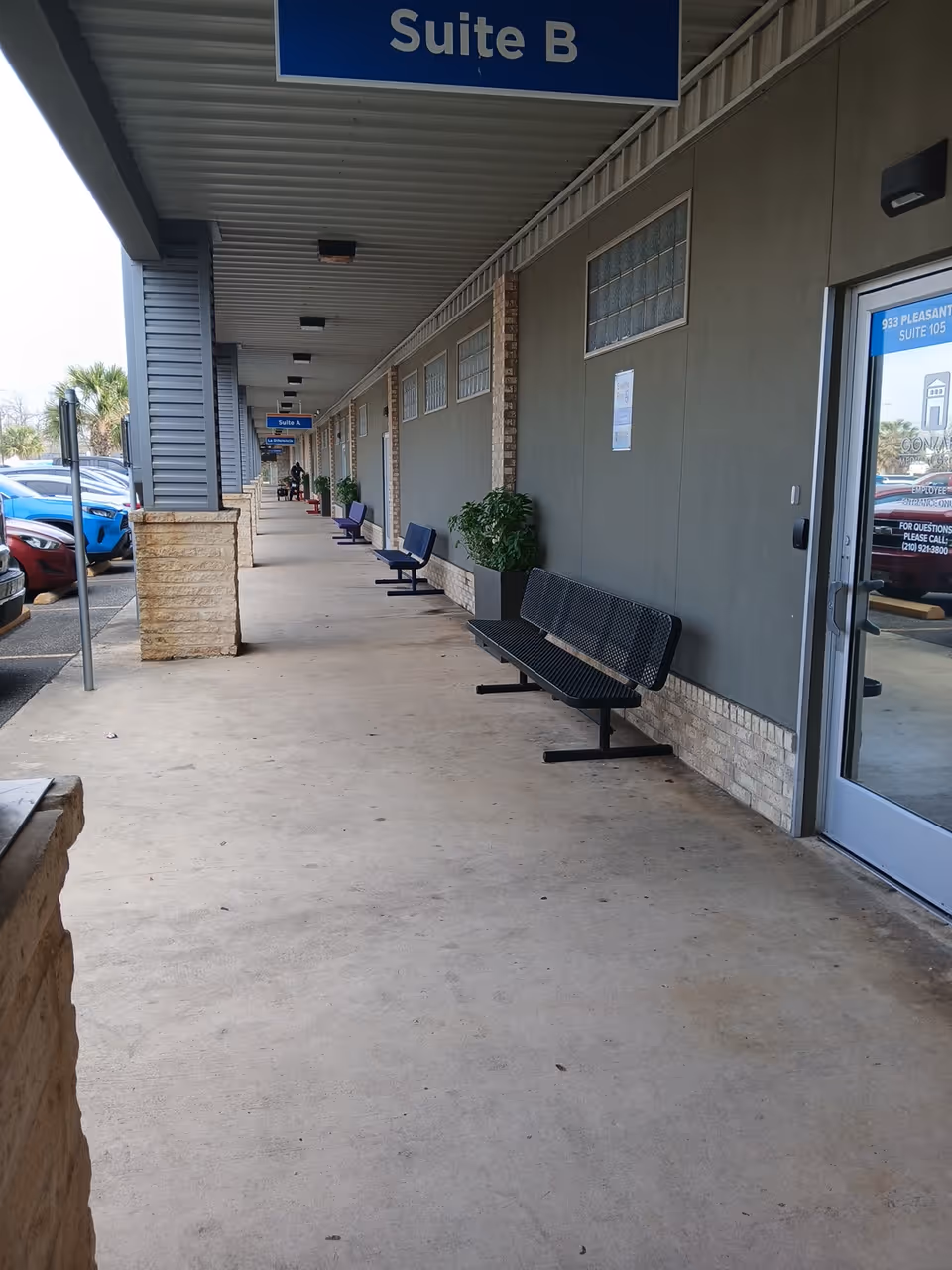 Outdoor hallway of a senior facility with benches, planters, and a glass entrance.