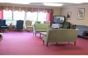 Cozy lounge area with pink carpet, sofas, chairs, and a TV by large windows.