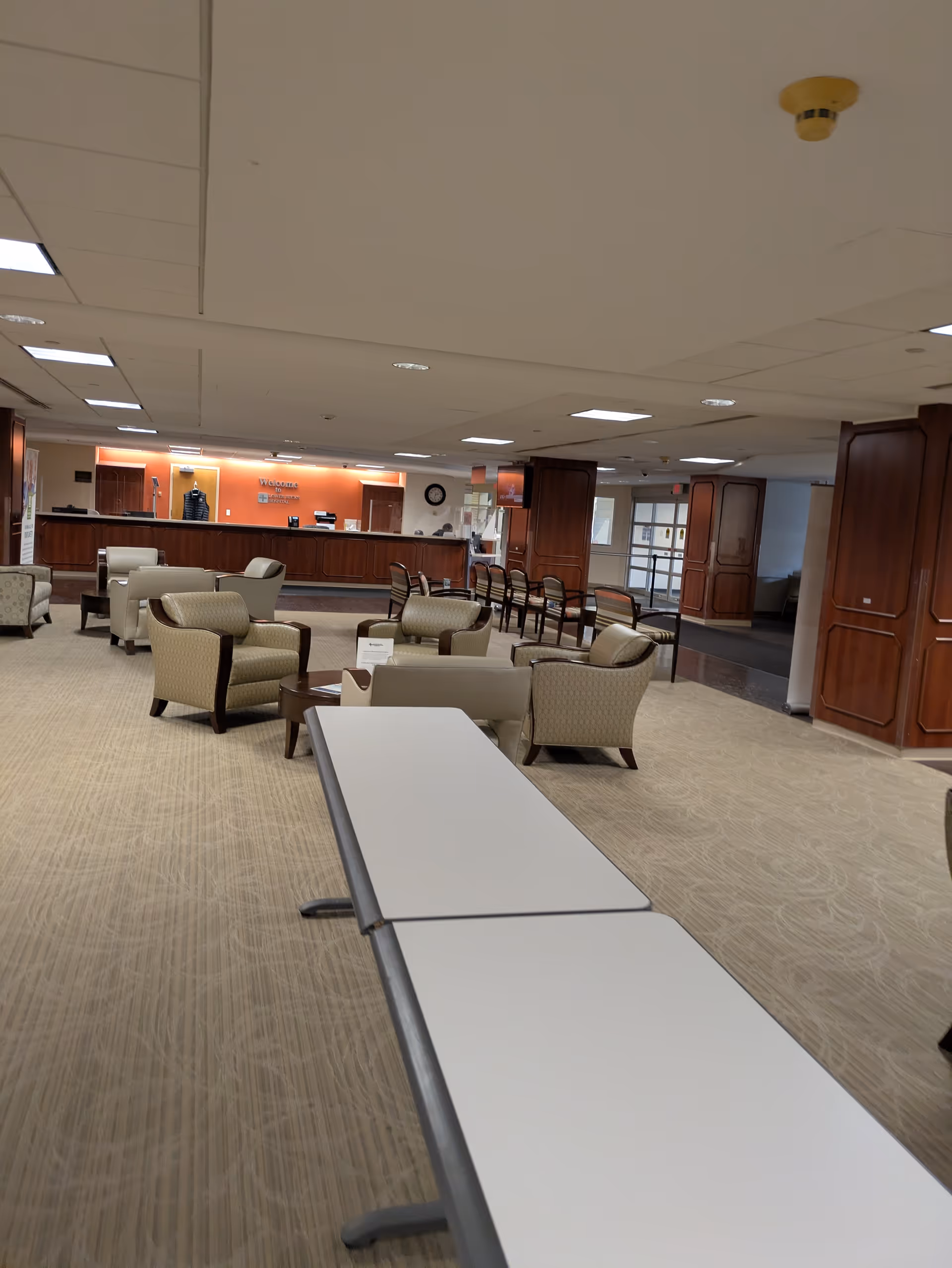 Senior living lobby with beige seating, long tables, and a reception desk.