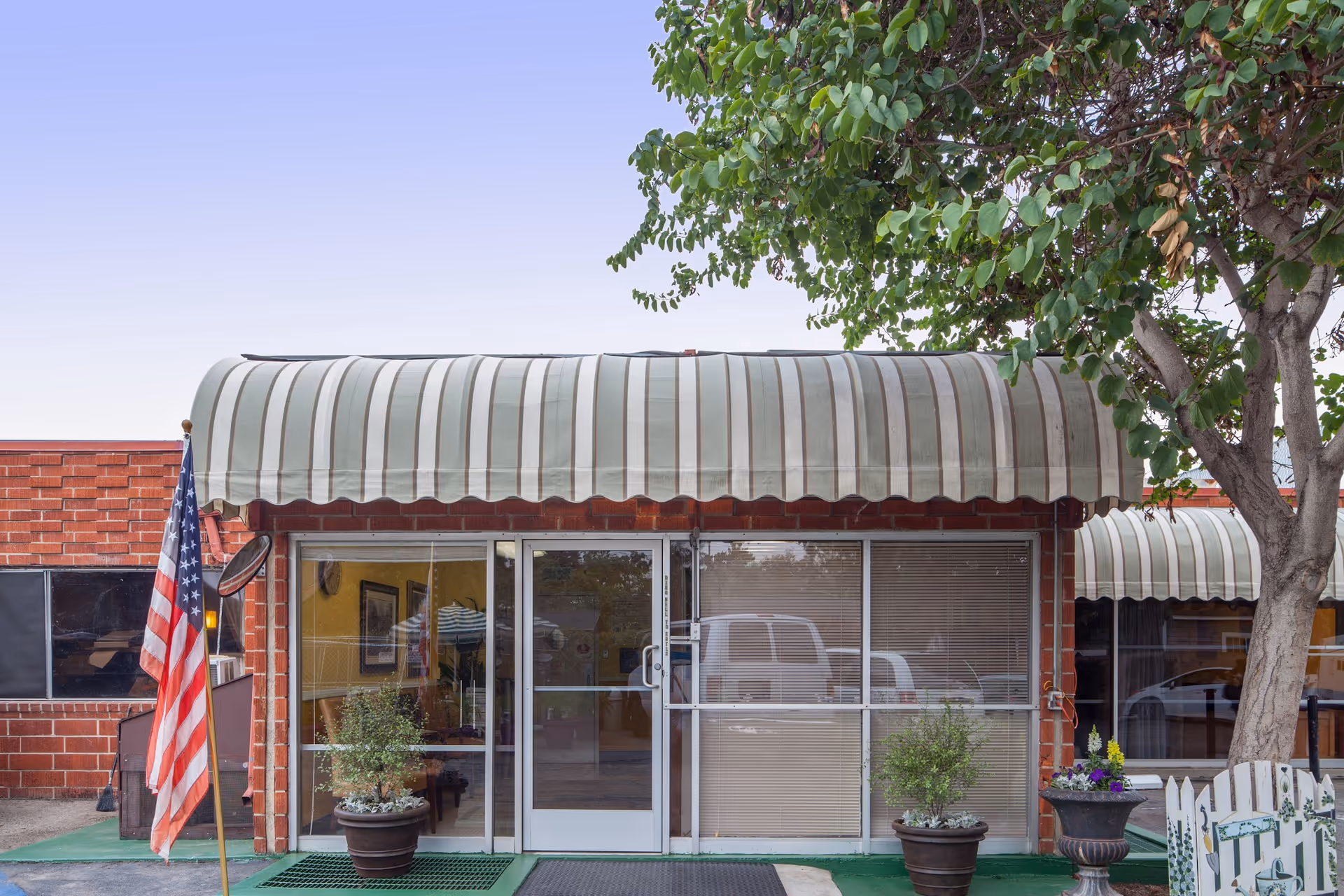 Meadowbrook Behavioral Health Center storefront with striped awnings, glass entrance, flag, and potted plants.
