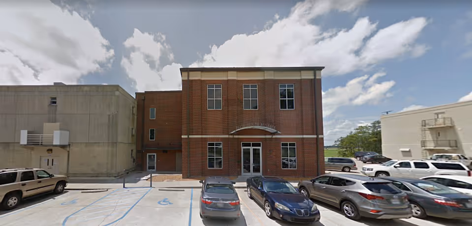 Front exterior of a brick, two-story Delta Health Alliance facility with cars.