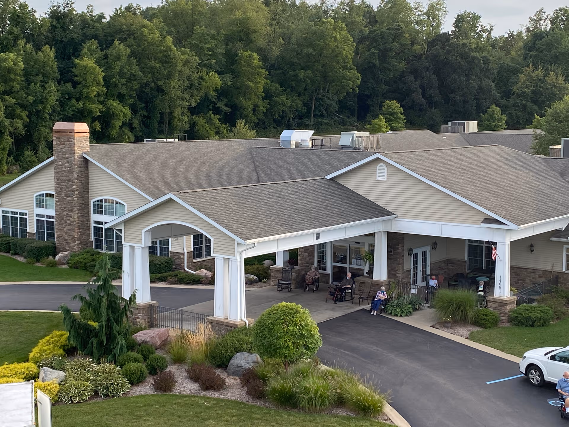 A senior living facility exterior with a covered entrance and residents seated outside.