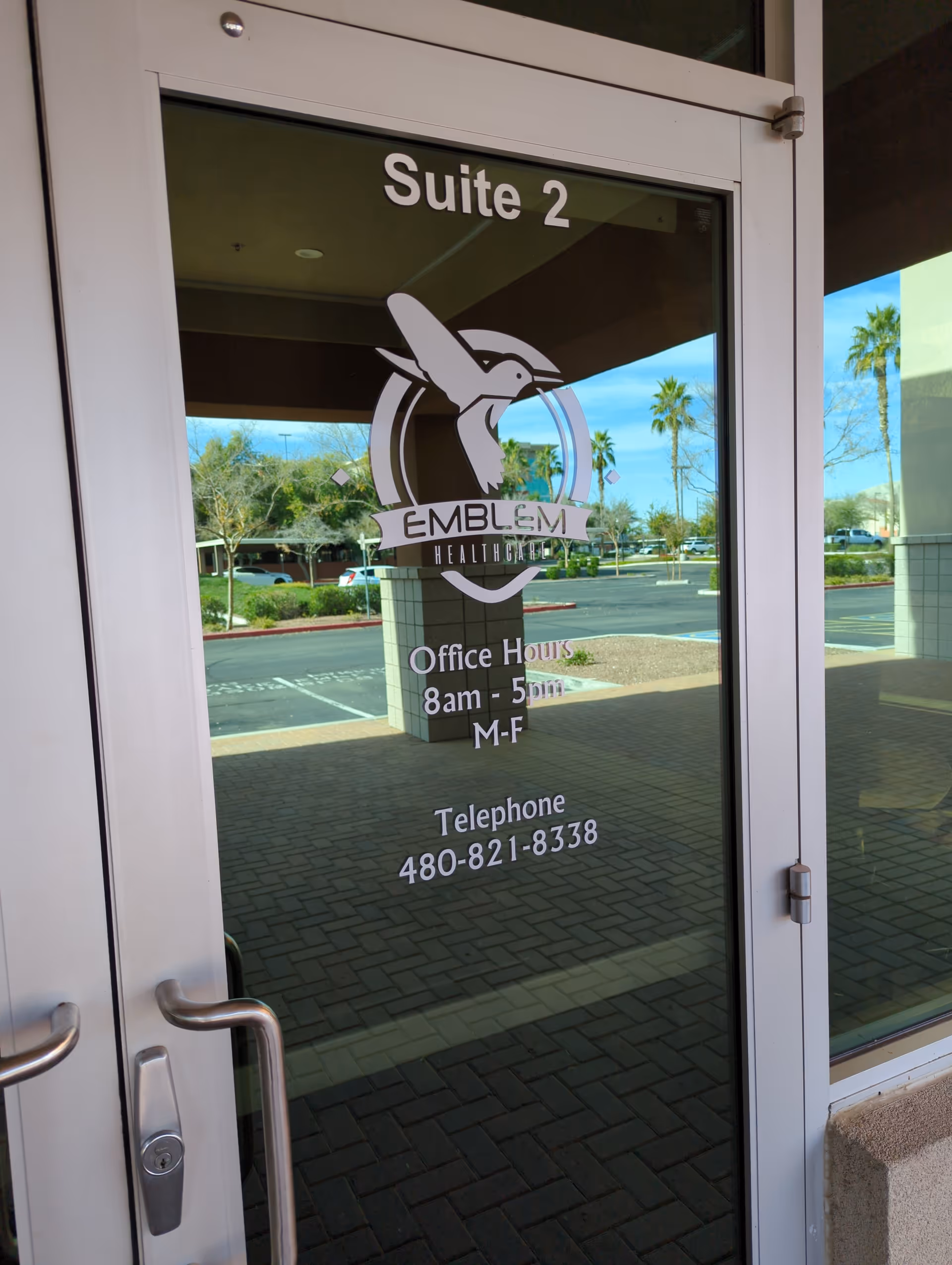 Glass entrance door for Emblem Healthcare displaying Suite 2 and office hours.