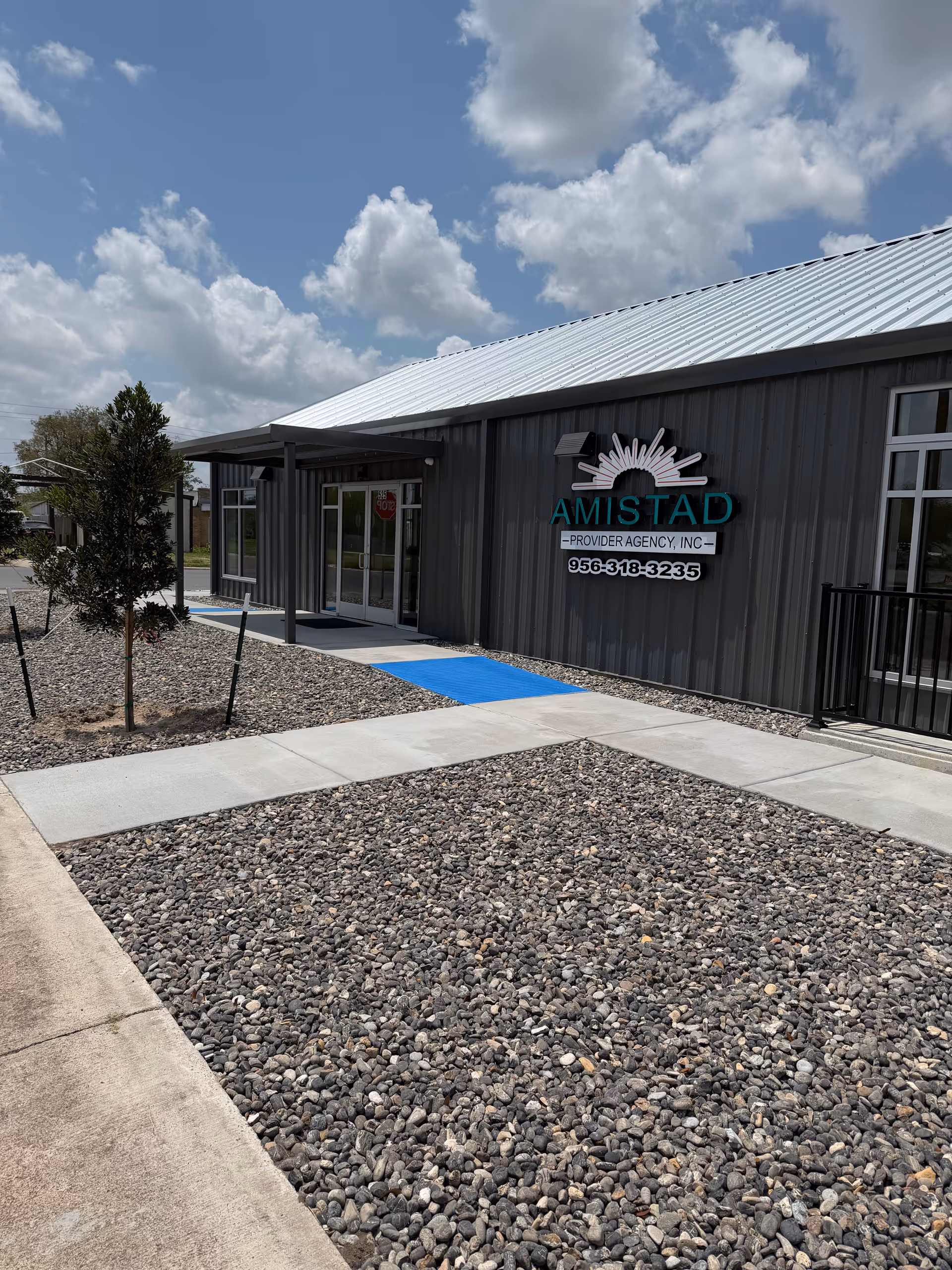 Exterior view of Amistad Provider Agency entrance with blue ramp and gravel landscaping.