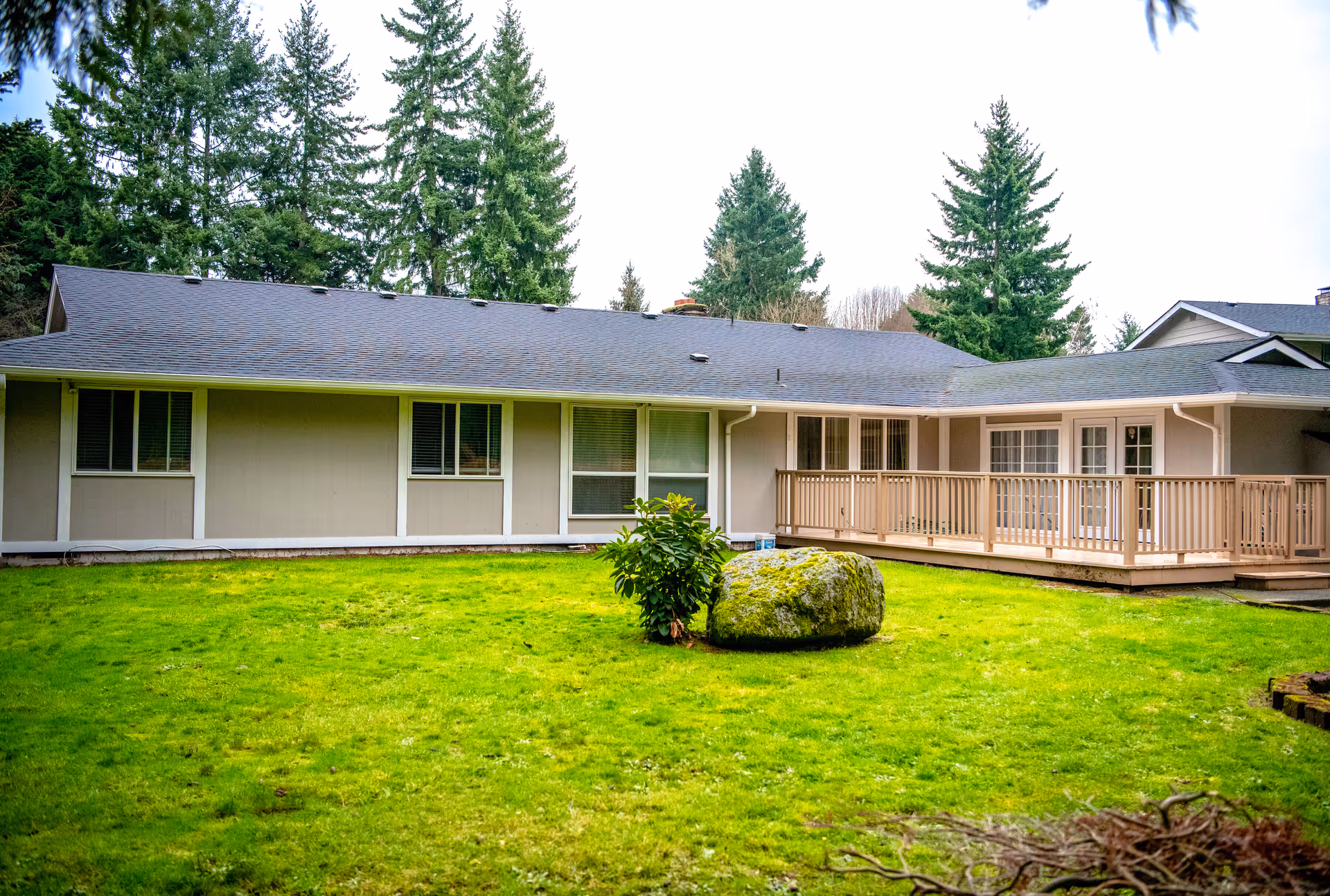 Single-story senior living facility exterior with beige walls, green lawn, and a wooden deck.