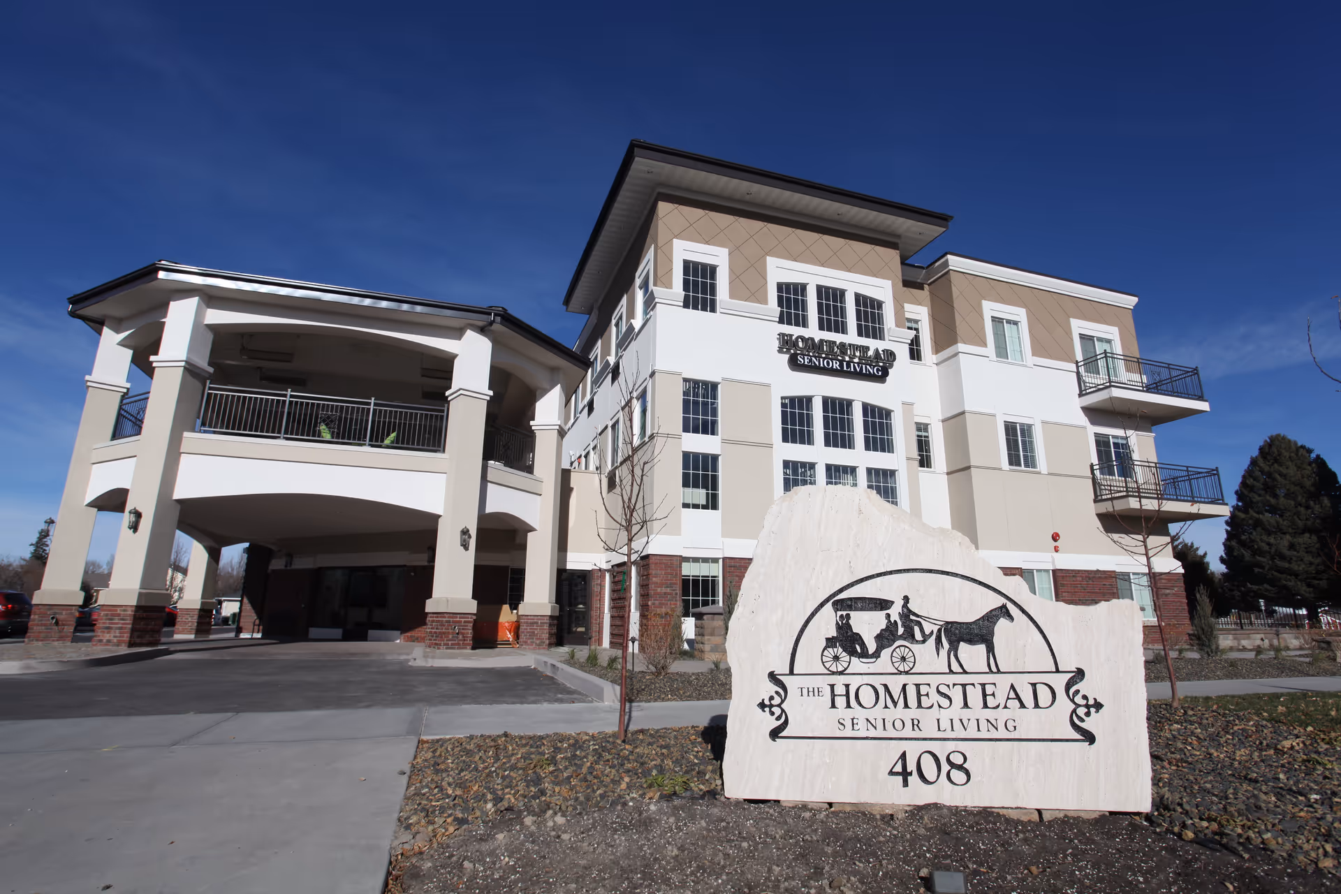 Three-story Homestead Senior Living building with beige facade and a large stone sign in front.
