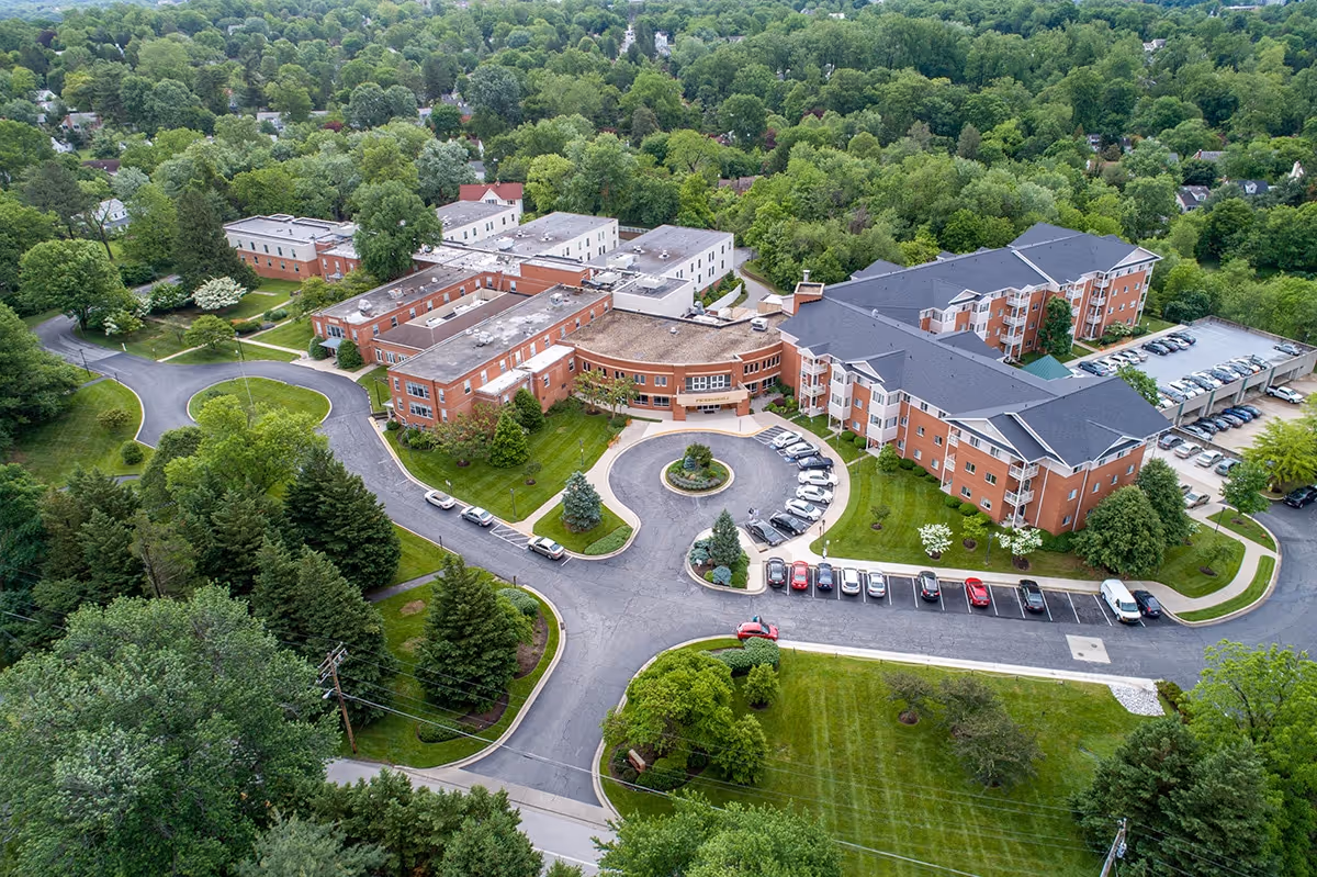 Aerial view of Pickersgill Retirement Community showing red-brick residential buildings, a circular driveway with parked cars, and surrounding trees.